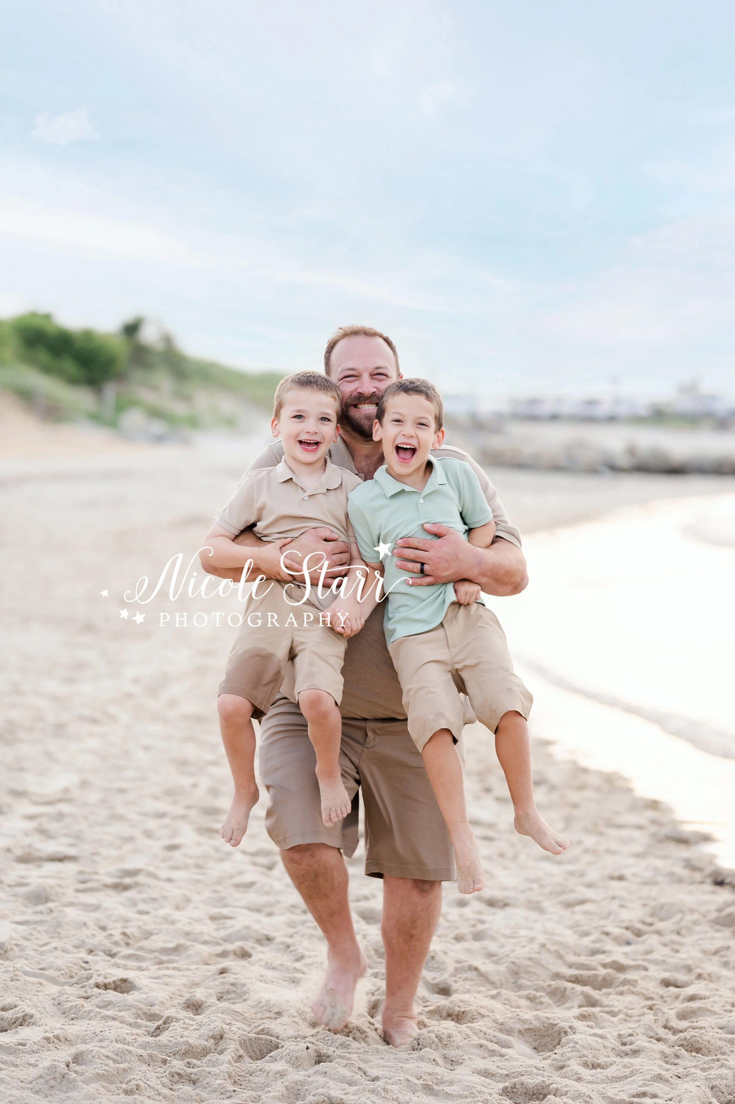 dad carries sons along sand laughing during summer family portraits on Cape Cod with MA beach photographer Nicole Starr Photography