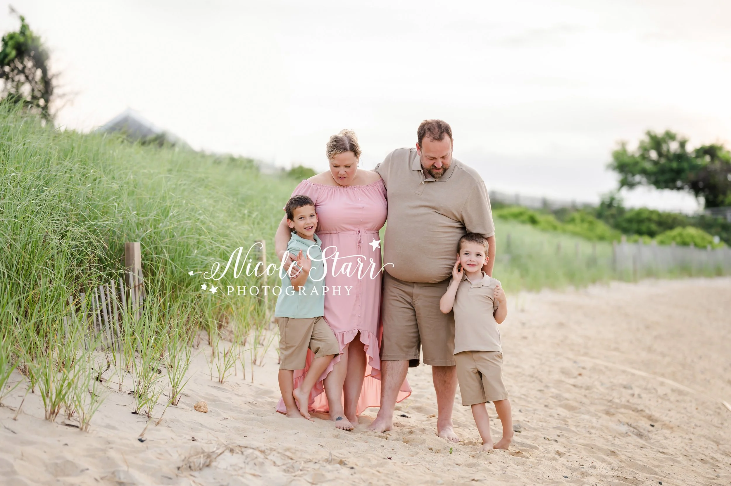 boys hug parents standing by sea grass and wooden fence on beach during summer Cape Cod extend family portraits with MA beach photographer Nicole Starr Photography