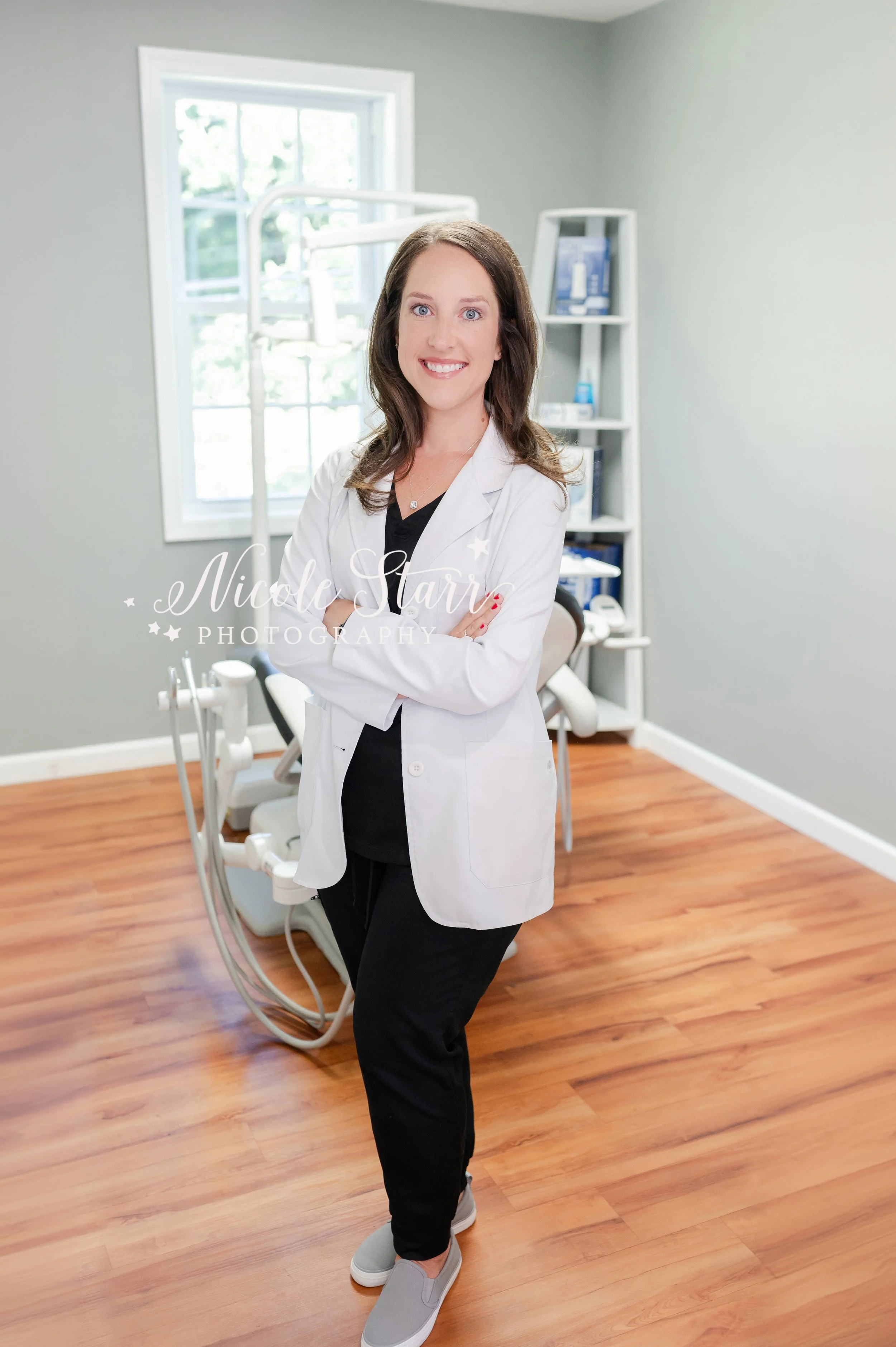 female dentist stands in office with arms crossed wearing white jacket during branding session in dental office photographed by Clifton Park branding photographer Nicole Starr Photography