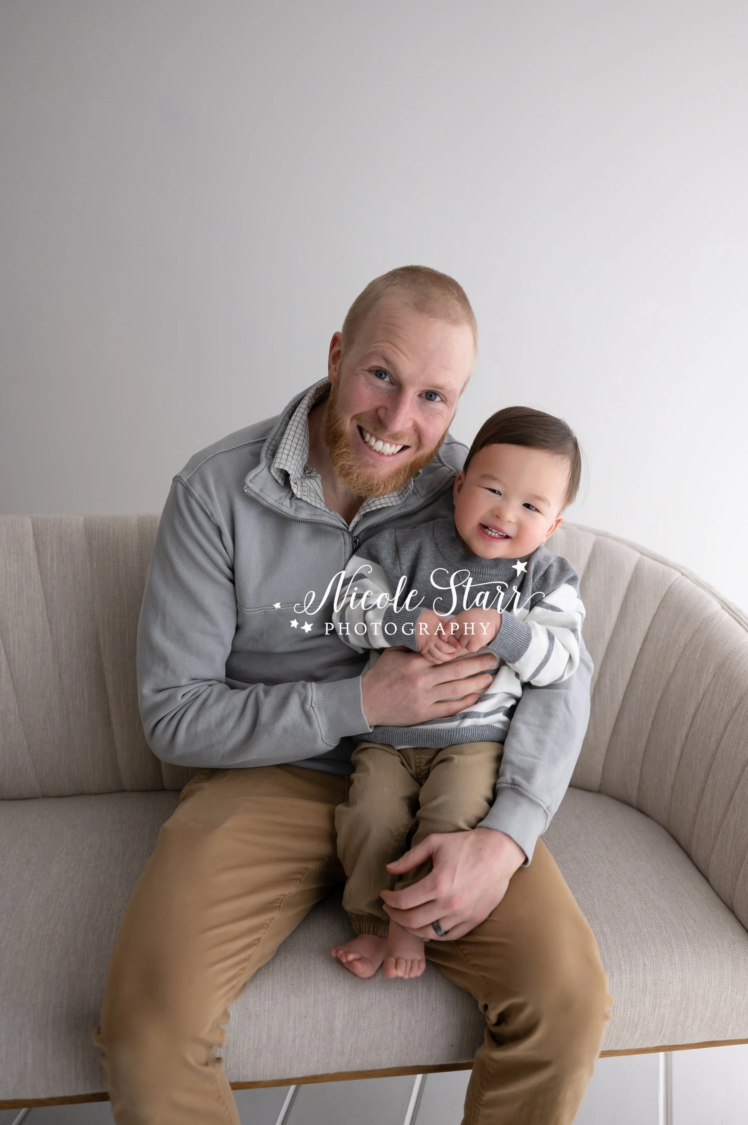 dad and toddler sit on sofa during family portraits in studio with Saratoga Springs NY family photographer Nicole Starr Photography
