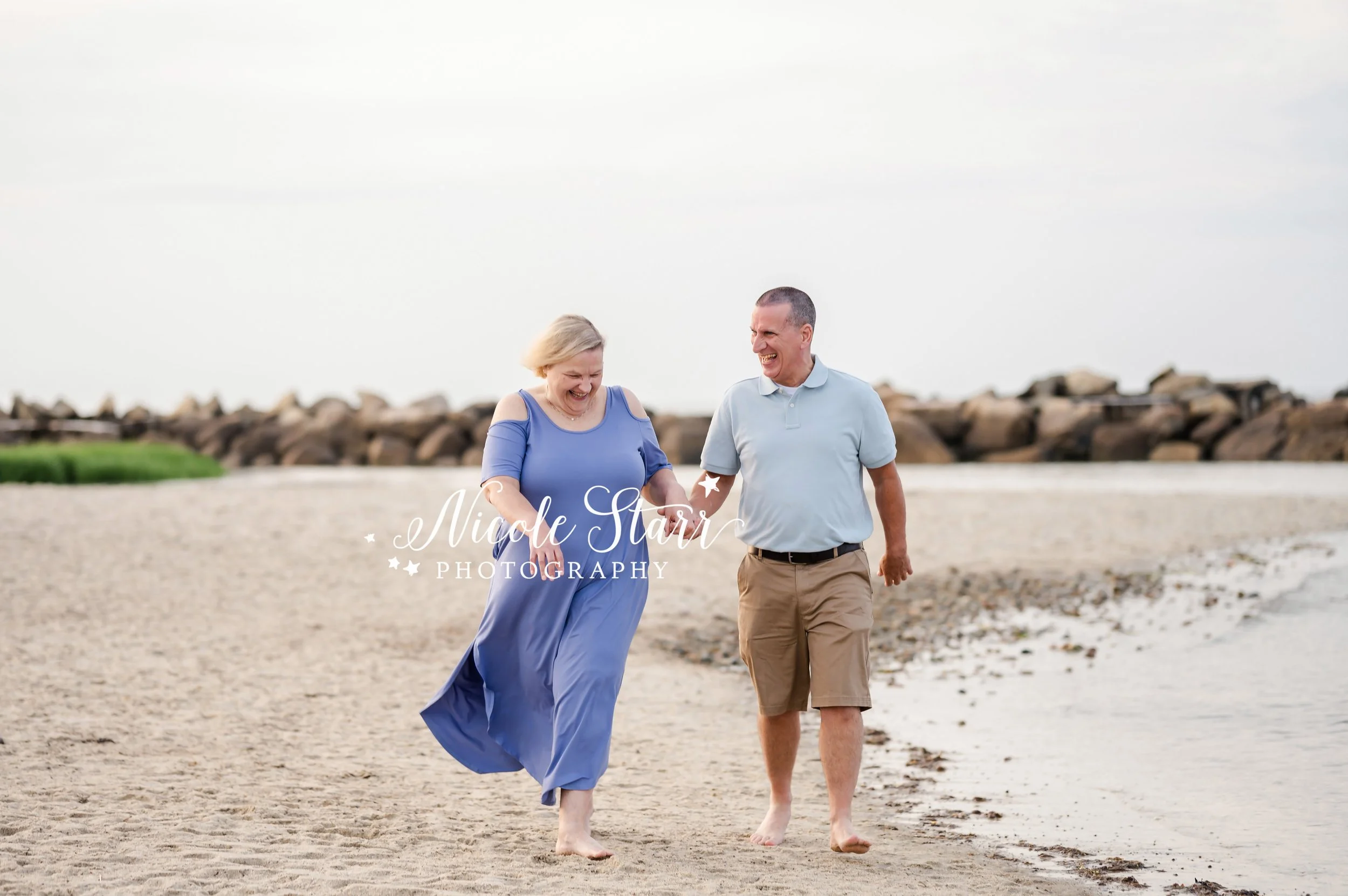 couple holds hands walking along beach waterfront during summer Cape Cod extend family portraits with MA beach photographer Nicole Starr Photography