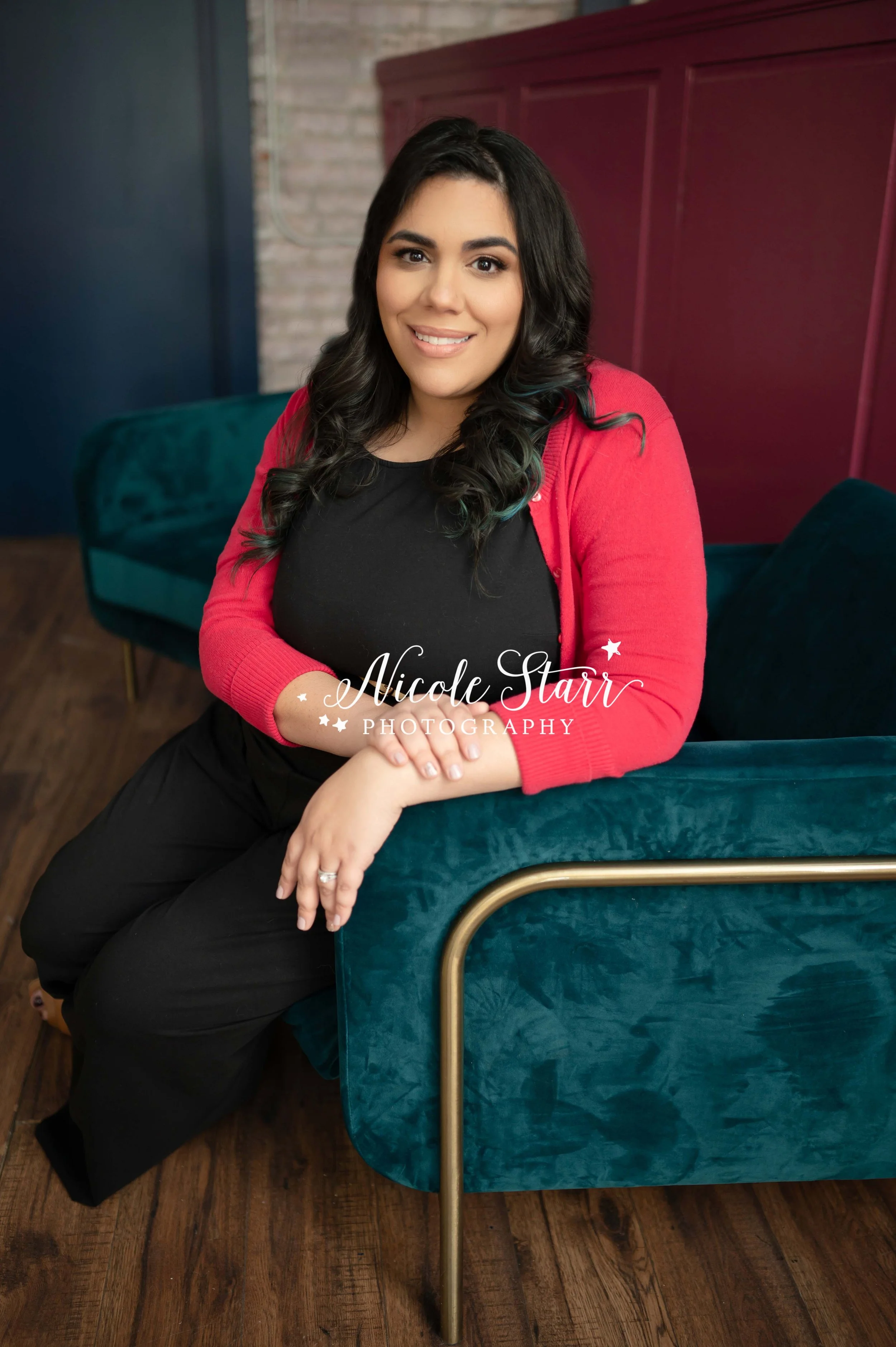 teacher sits in black pantsuit with bright pink sweater in teal velvet chair during headshots at Palette Community in Schenectady NY photographed by New York headshot photographer Nicole Starr Photography