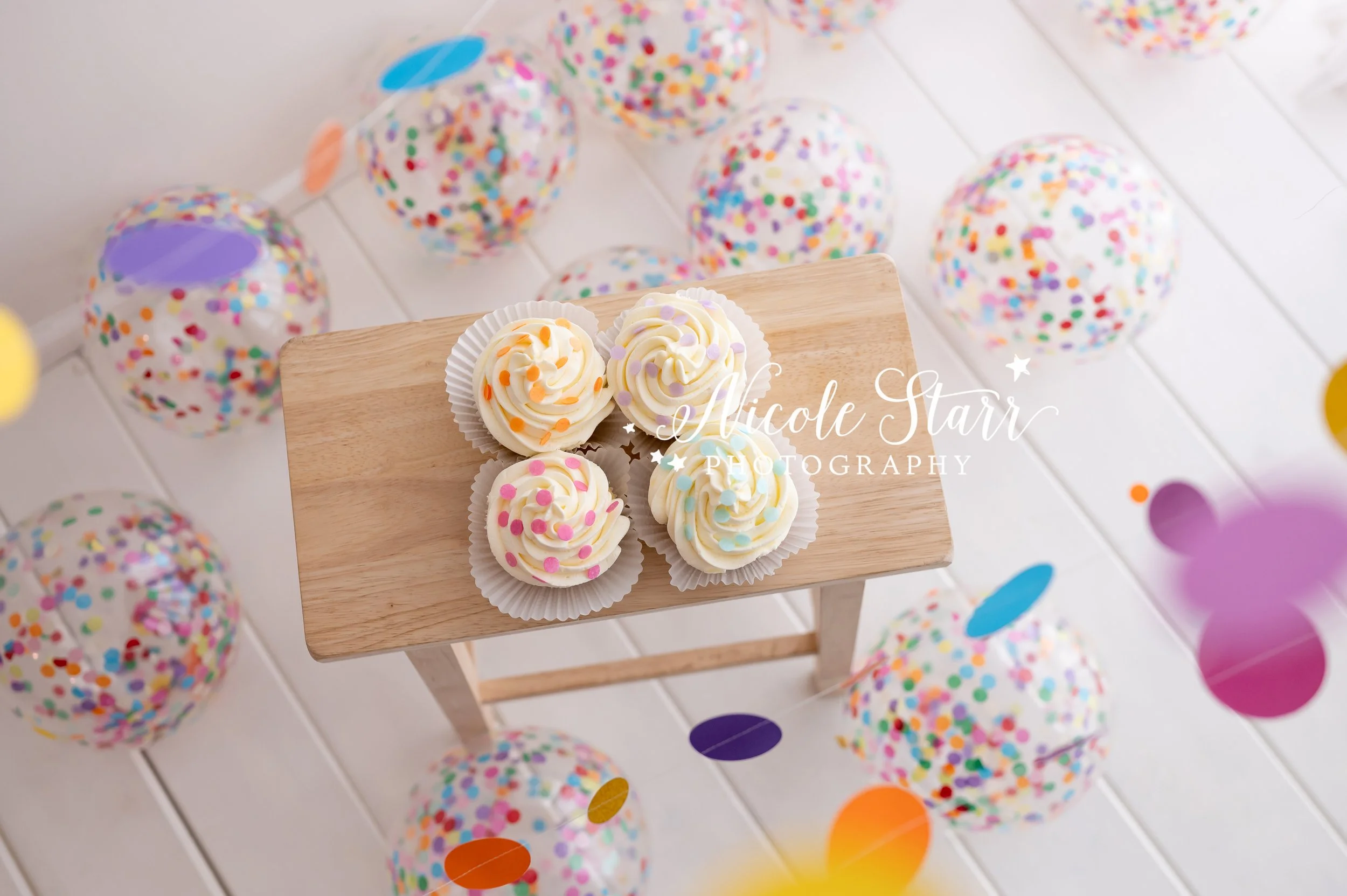 four confetti cupcakes for cake smash with friends in front of rainbow streamers in Saratoga Springs studio with Nicole Starr Photography