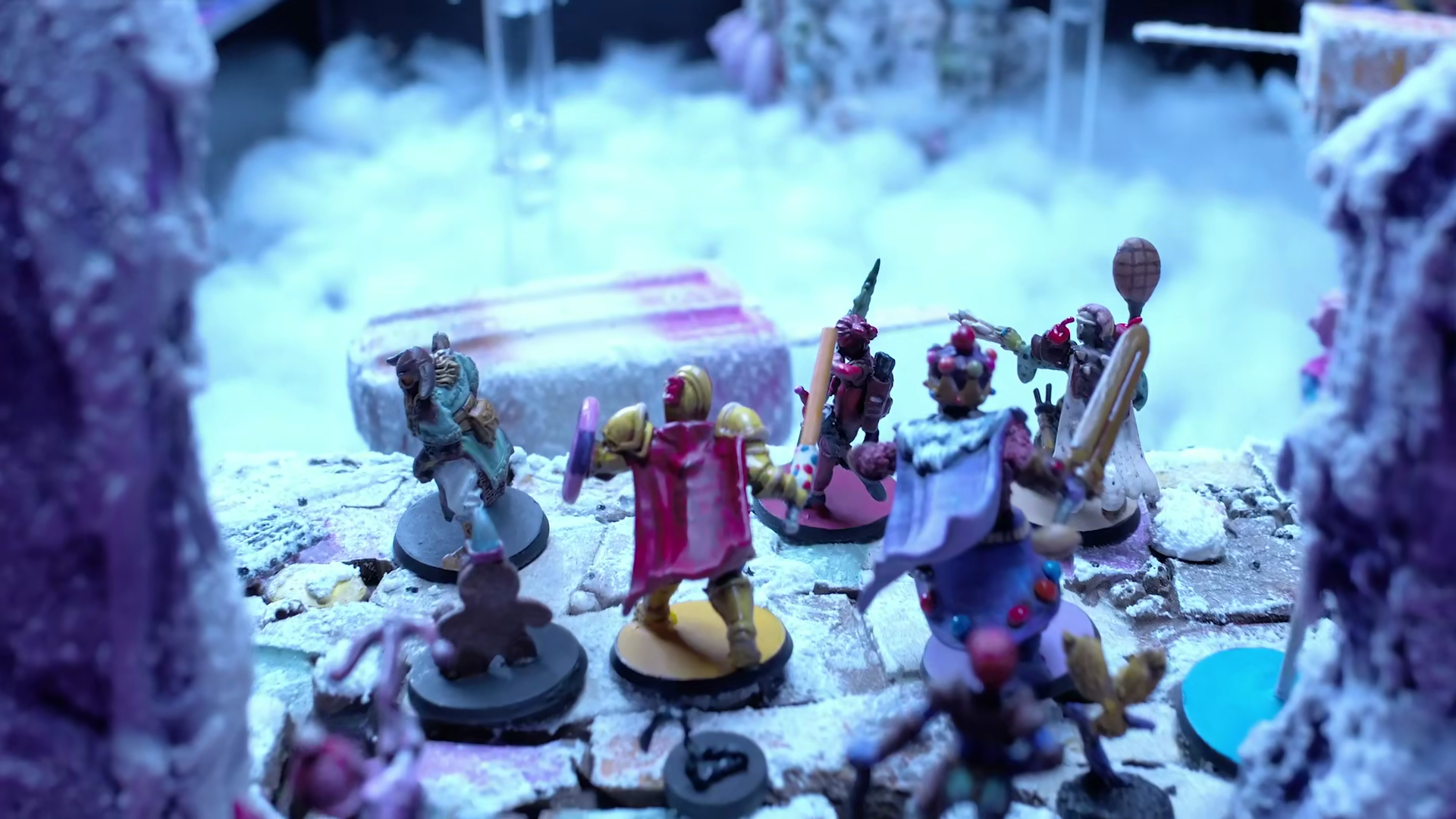 Miniature fantasy figures, including armored characters and a horse, are arranged on a snowy surface with winter-themed scenery in the background.