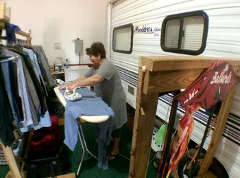 A women Ironing her and her husbands clothes, inside the RV they share, after leaving their home to find employment in Watford City ND. (Credit: Tom Haines )