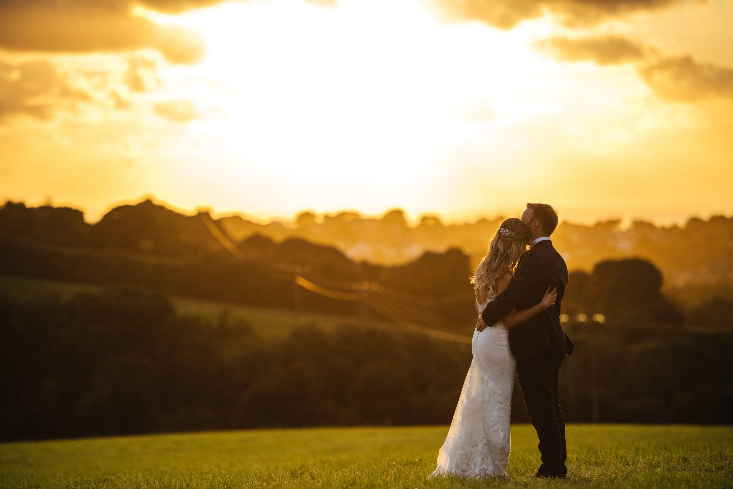 Bride and groom kissing at sunset in a field