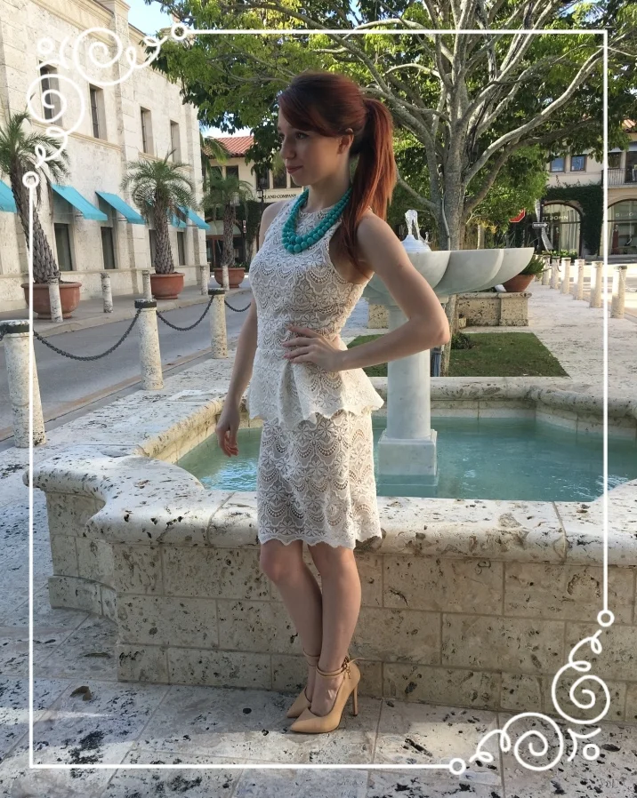 Jessie is rocking a high pony and wearing a white lace peplum dress by Guess, a chunky blue double-strand necklace, and pointy toed nude pumps.