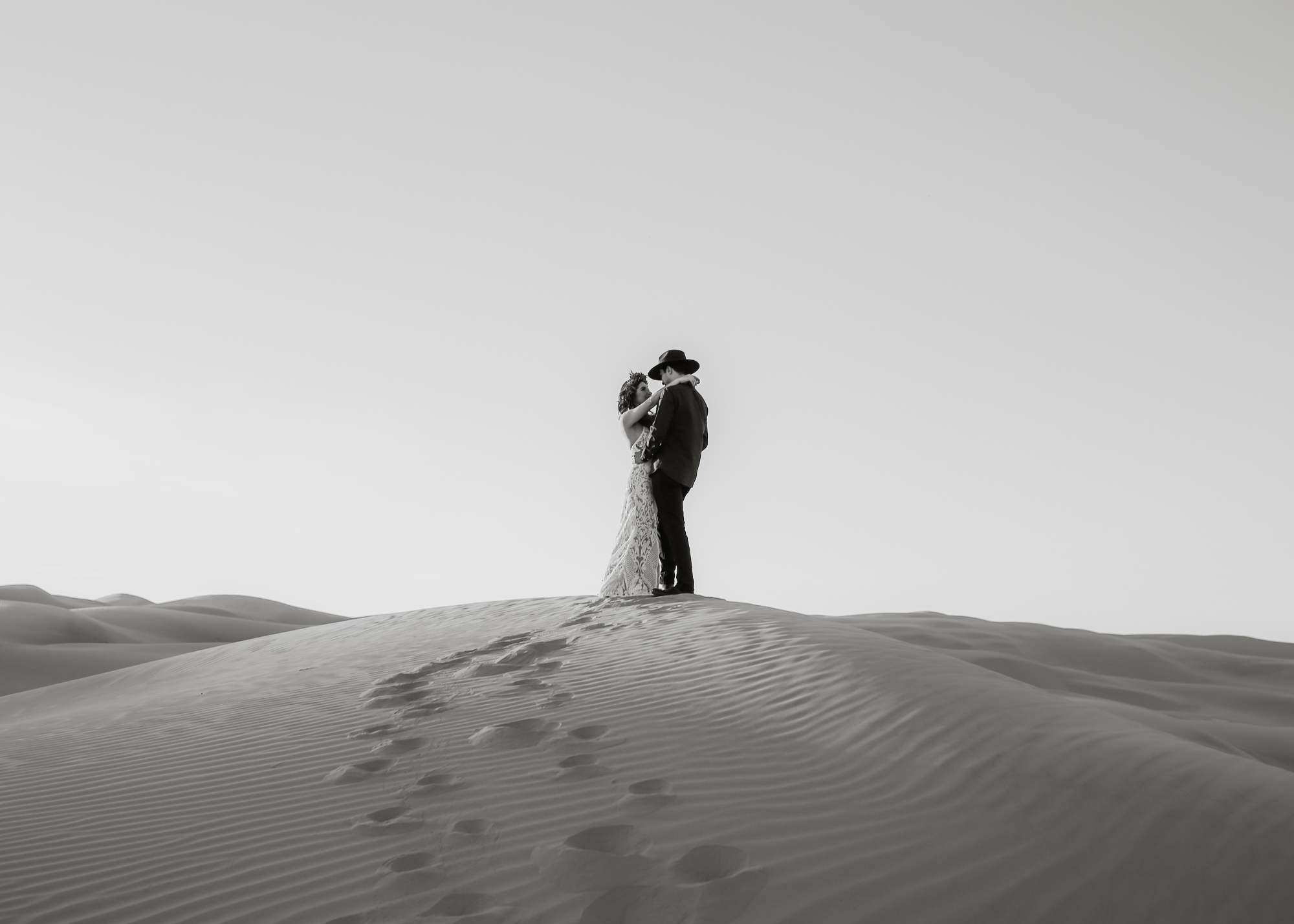 Una pareja en un desierto, abrazados y mirándose. La escena es en blanco y negro.