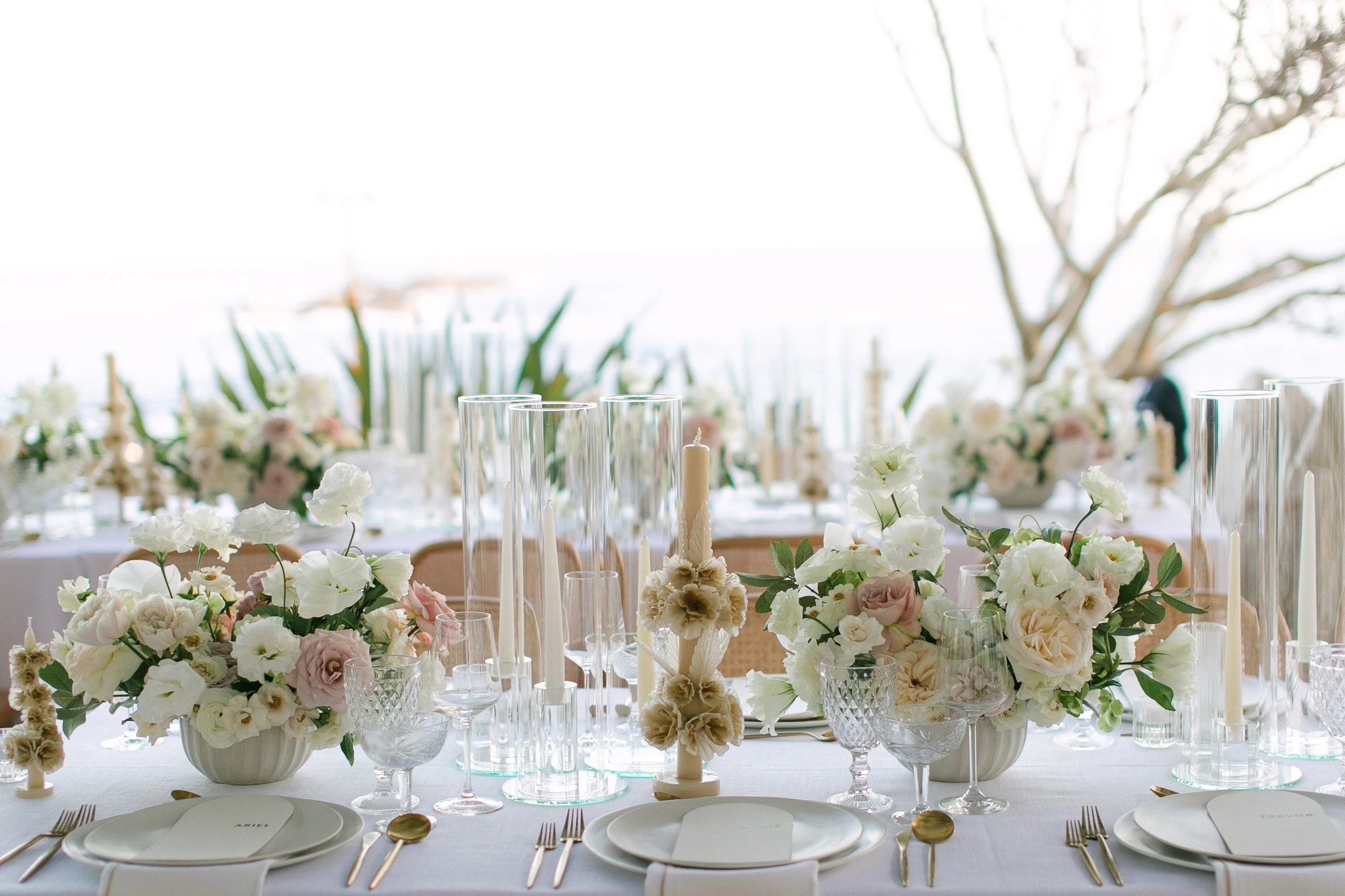 Mesa de banquete decorada con arreglos florales en tonos pastel, candelabros y cristalería.