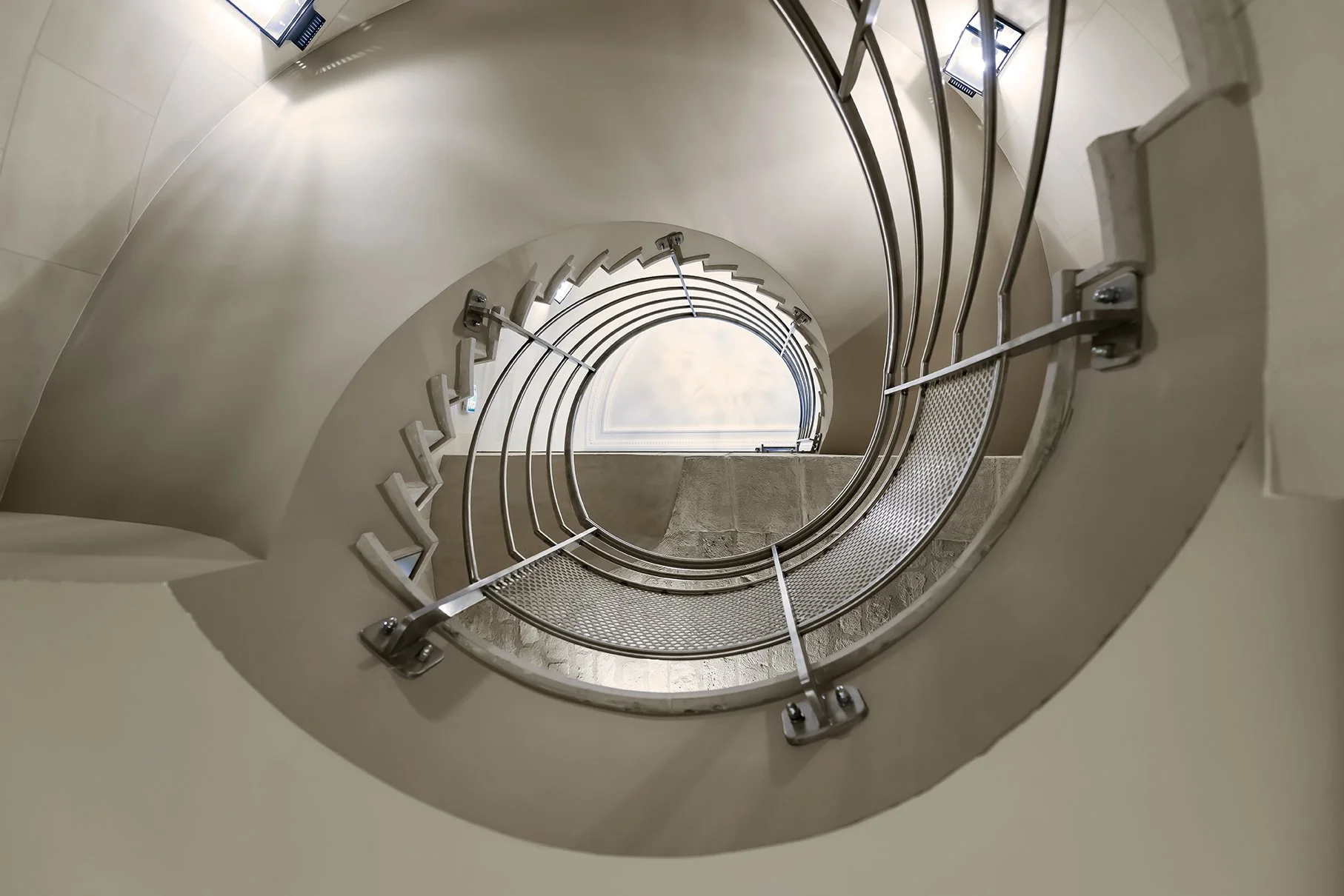 Vue du bas d'un escalier spiral qui descend vers un plafond lumineux. Cercle d'Aumale, hôtel particulier, Paris, Location, Prestige, Luxe, Dalida,
