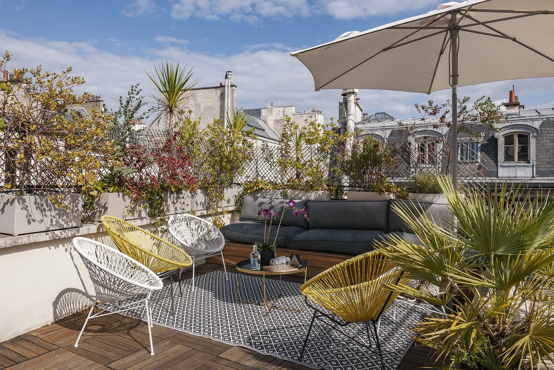 Terrasse urbaine avec mobilier moderne, plantes en pot, parasol beige, et un ciel partiellement nuageux, Cercle d'Aumale, hôtel particulier, Paris, Location, Prestige, Luxe, Dalida, soleil, 