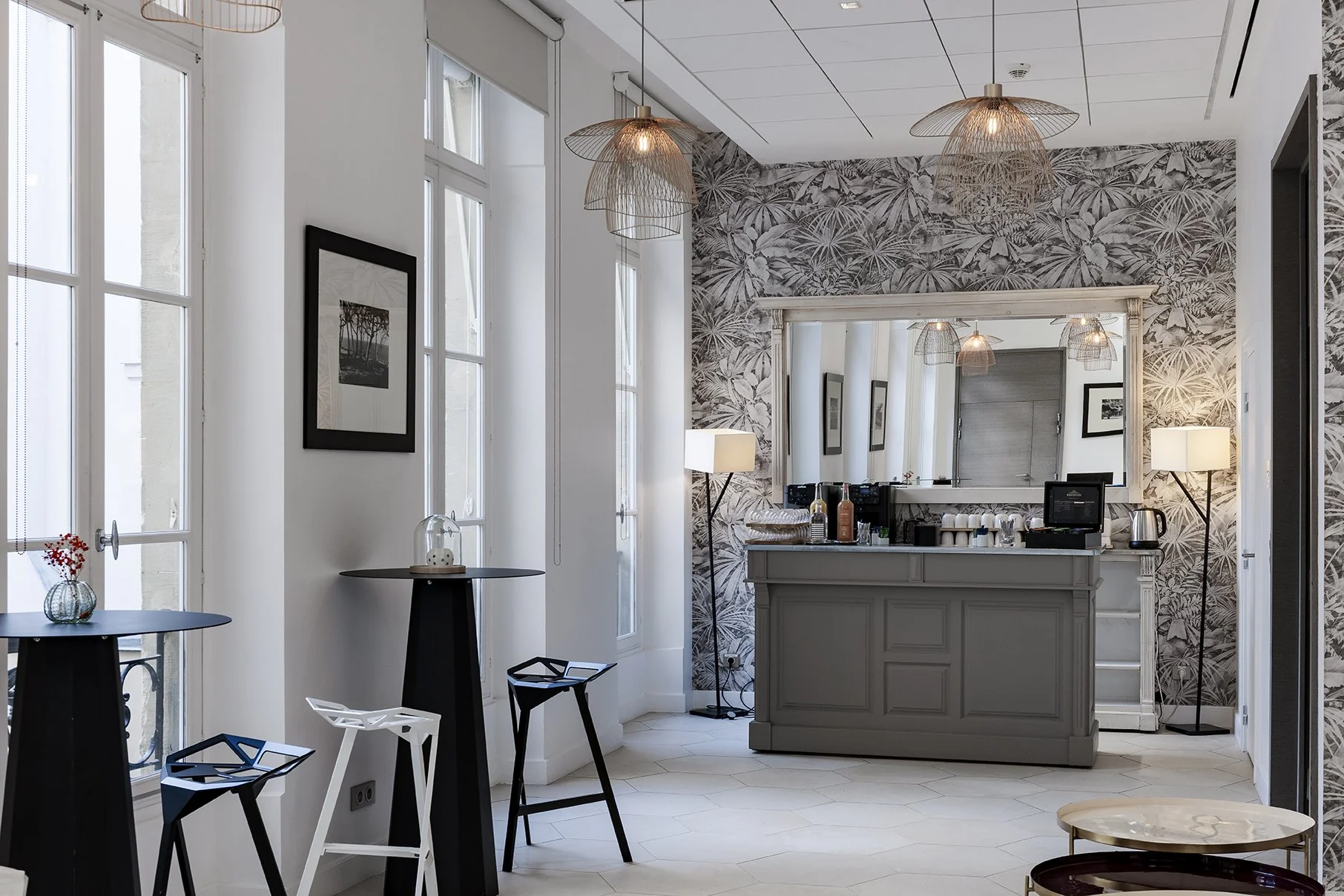 Intérieur moderne avec des tables noires, chaises design, un mur avec papier peint végétal, un grand miroir, et un comptoir bar avec des appareils électriques, Cercle d'Aumale, hôtel particulier, Paris, Location, Prestige, Luxe, Dalida,
