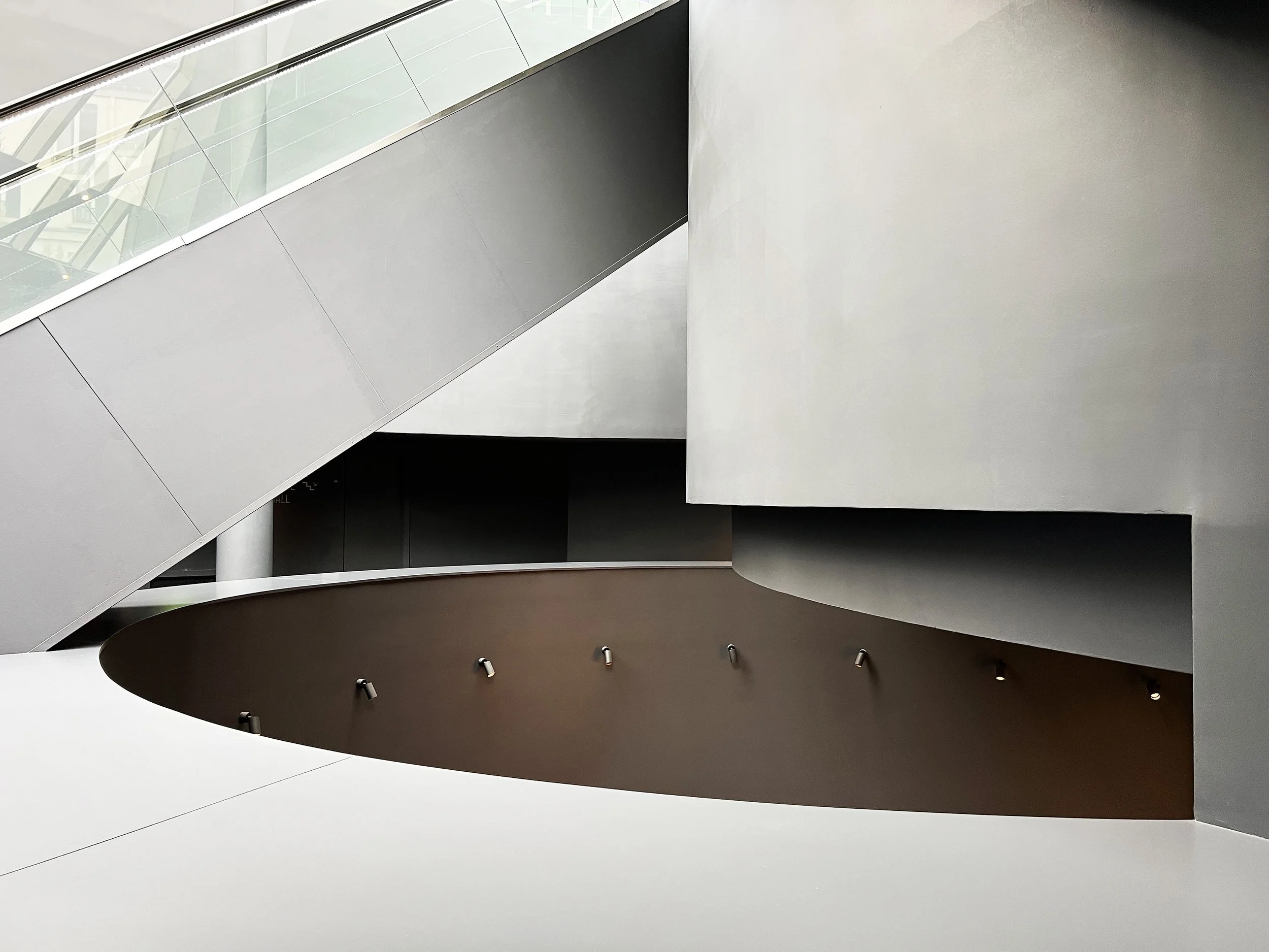 Vue intérieure d'un bâtiment moderne avec des murs blancs, un escalier suspendu en métal et verre, des éclairages encastrés, et une architecture minimaliste, Paris,