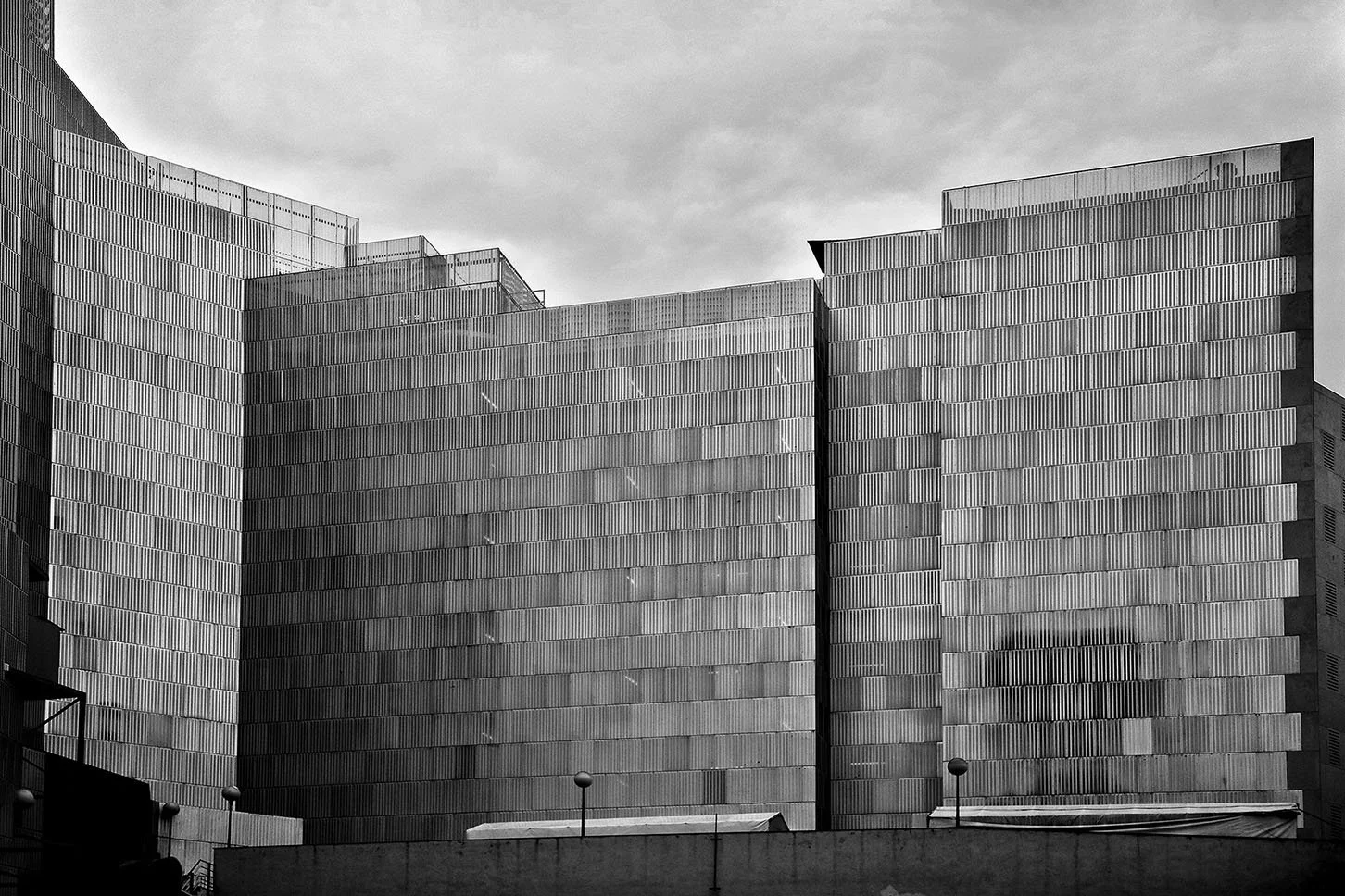 Bâtiment moderne en acier avec structure géométrique, sous un ciel nuageux. Barcelone, Espagne, architecture,