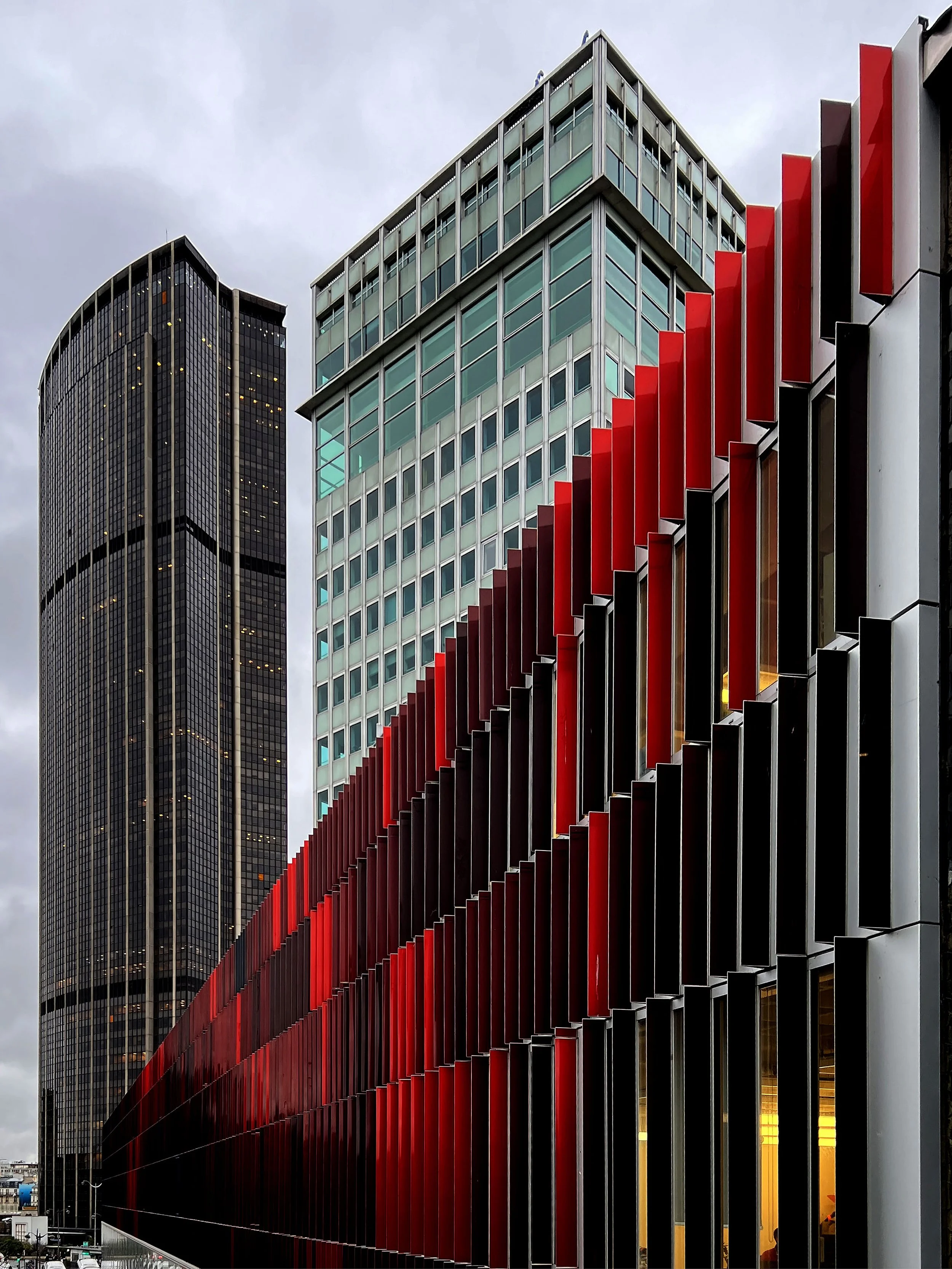 Photographie de gratte-ciel modernes avec une façade en verre et des éléments en rouge et noir, avec un ciel nuageux en arrière-plan.
Montparnasse, Paris, France, Architecture,
