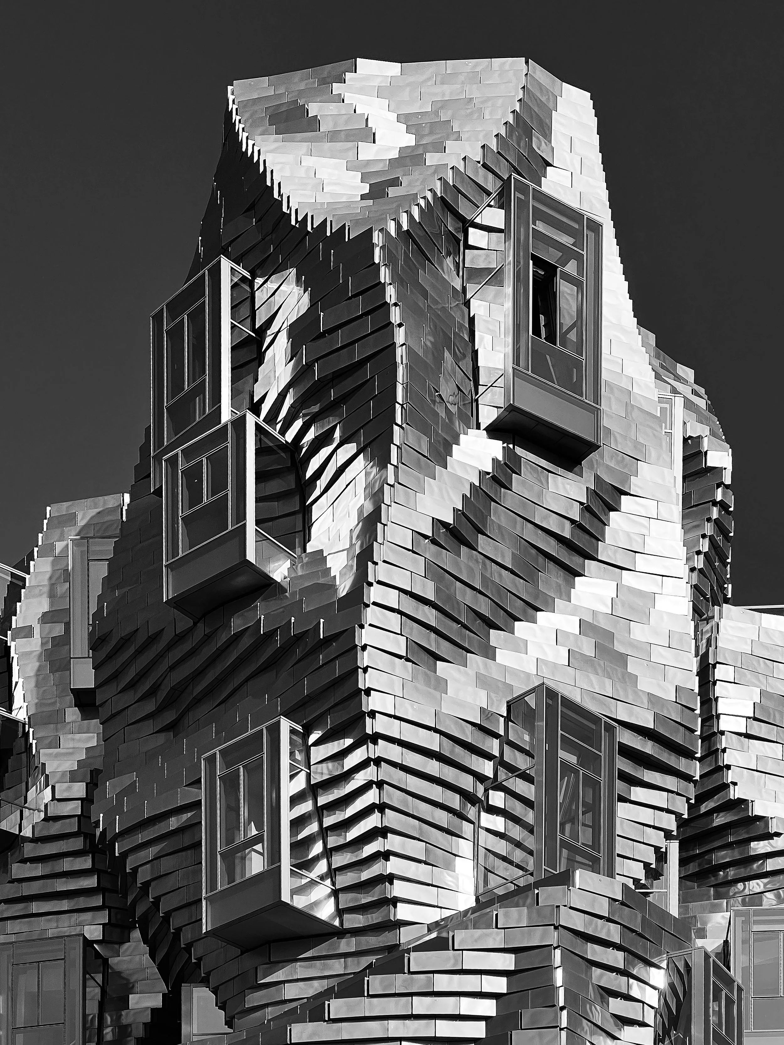 Un bâtiment moderne en acier et en verre avec une architecture complexe et angulaire, vu en noir et blanc, Luma, Arles, Gehry, Architecture.