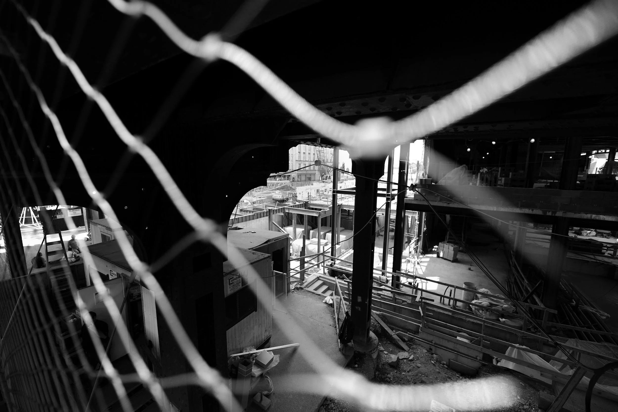 Vue d'un chantier de construction vu à travers une clôture en fil de fer, montrant des structures en cours d'assemblage, des équipements, et des bâtiments dans le fond. New-York, U.S.A, Workers,