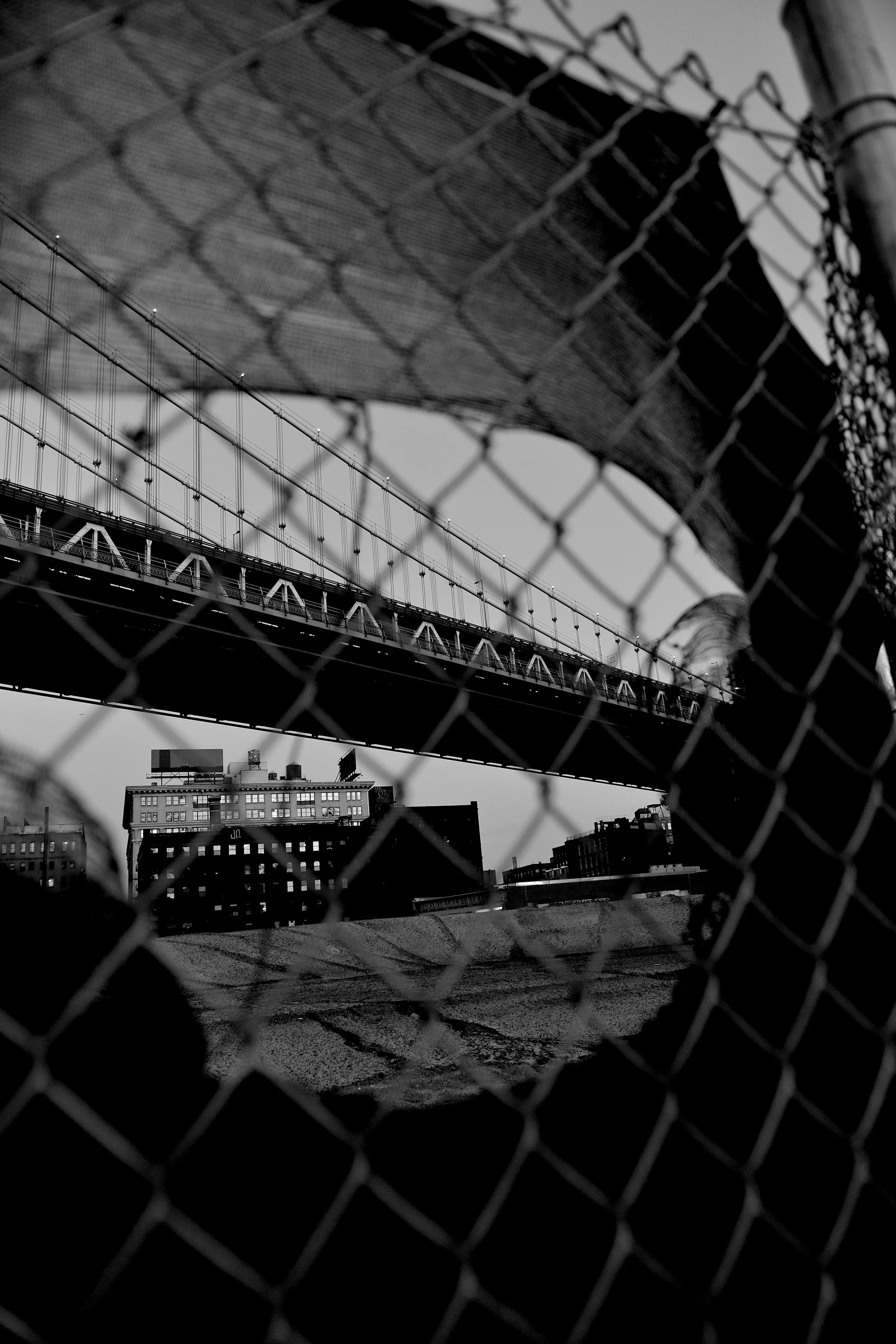 Une vue en noir et blanc de ponts suspendus au-dessus d'une ville, vue à travers une grille métallique. Architecture, Brooklyn, New-York, U.S.A, 