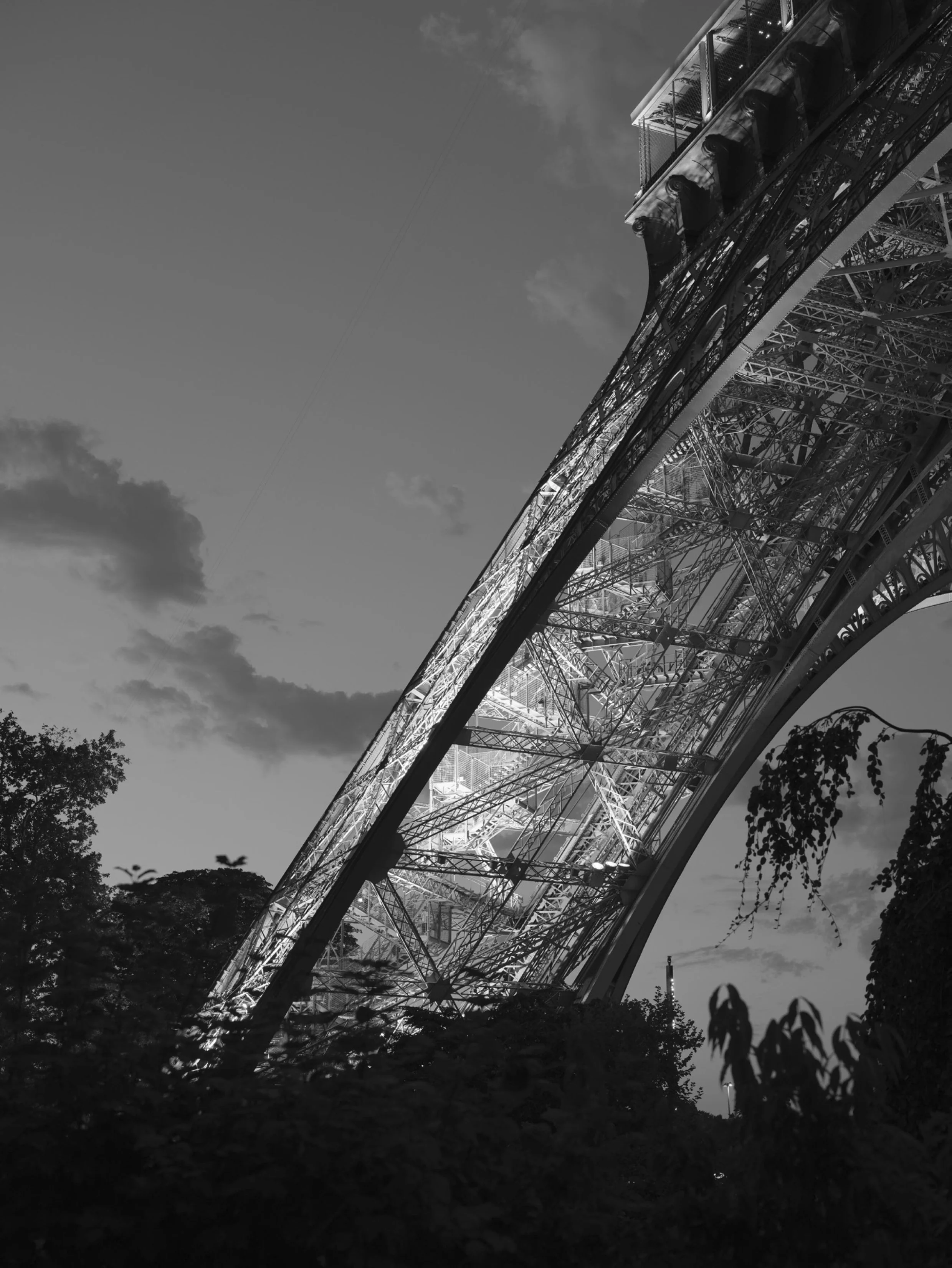 Pied Ouest de la Tour Eiffel, avec un éclairage, prise en contre-plongée, vue de dessous avec des arbres en premier plan et un ciel nuageux en arrière-plan. Paris, France, Architecture,