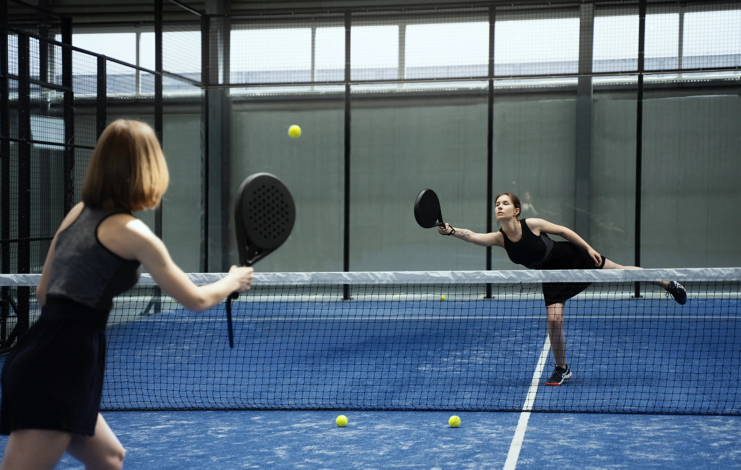 Padel player lunging for a low forehand on an indoor court in Singapore