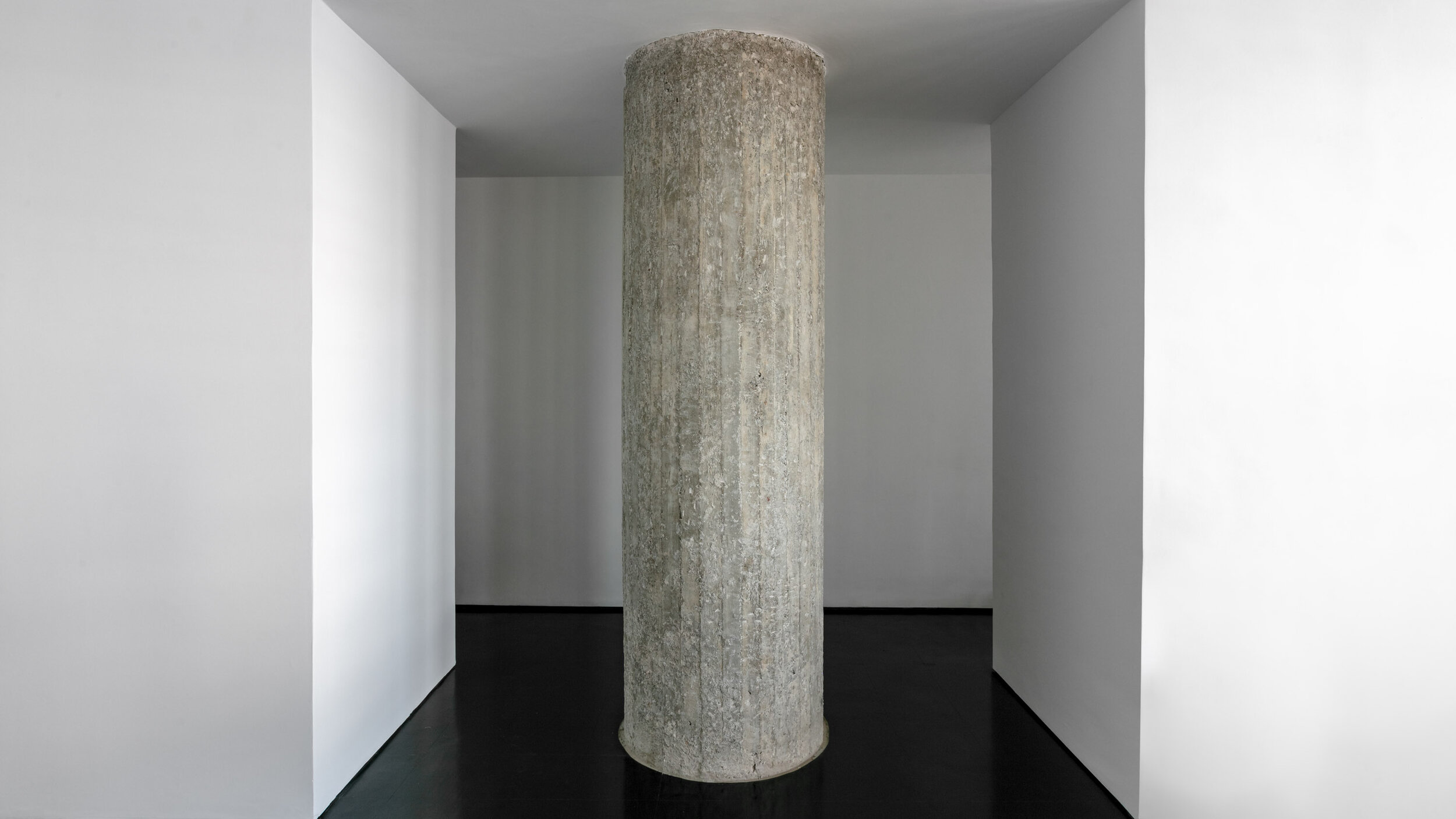 Concrete pillar in a minimalistic room with white walls and black floor.