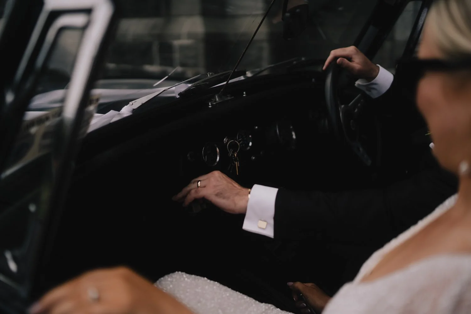 husband and wife in classic car, driving to reception after ceremony, his hand on the steering wheel