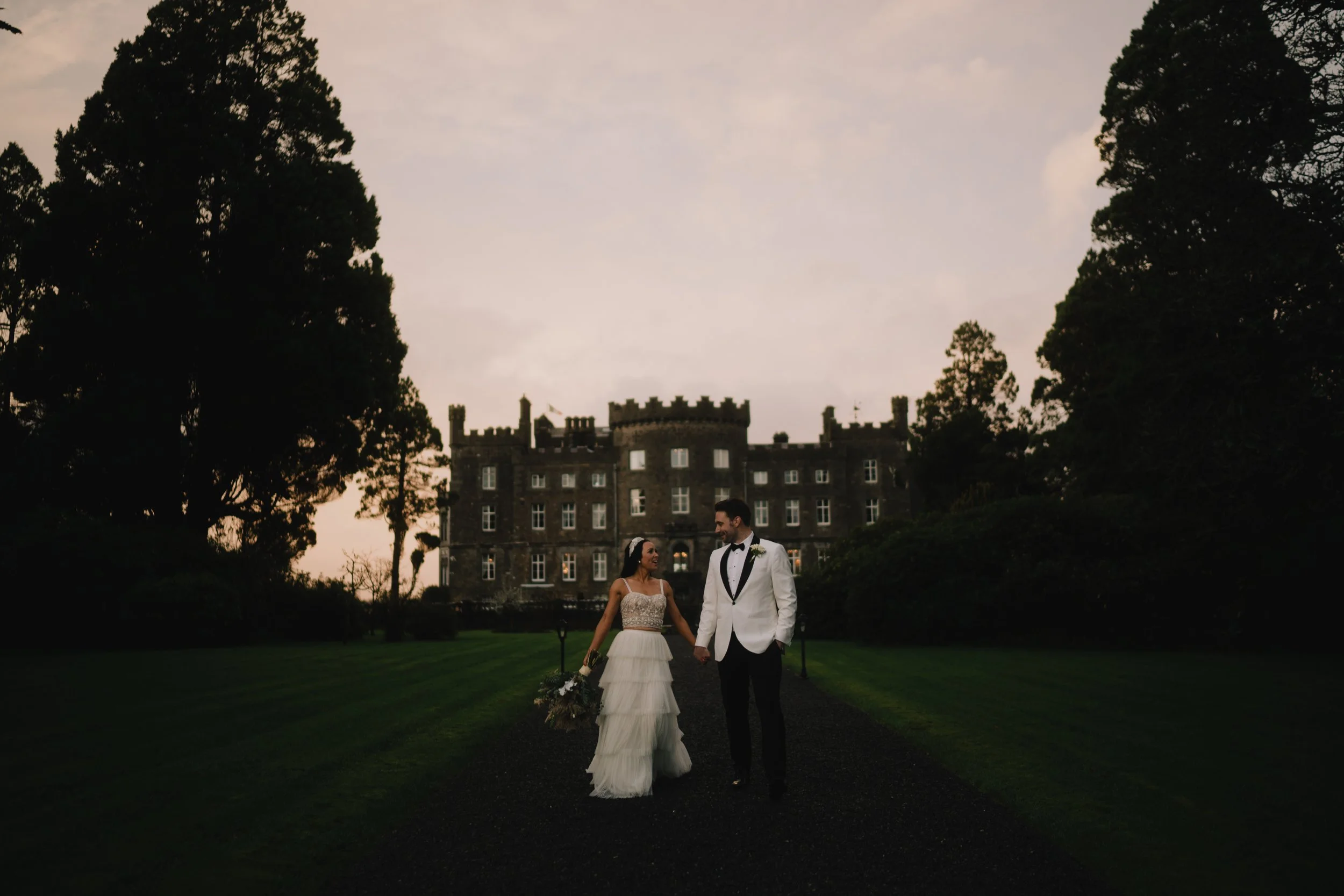 couple walk hand in hand with markee castle as backdrop