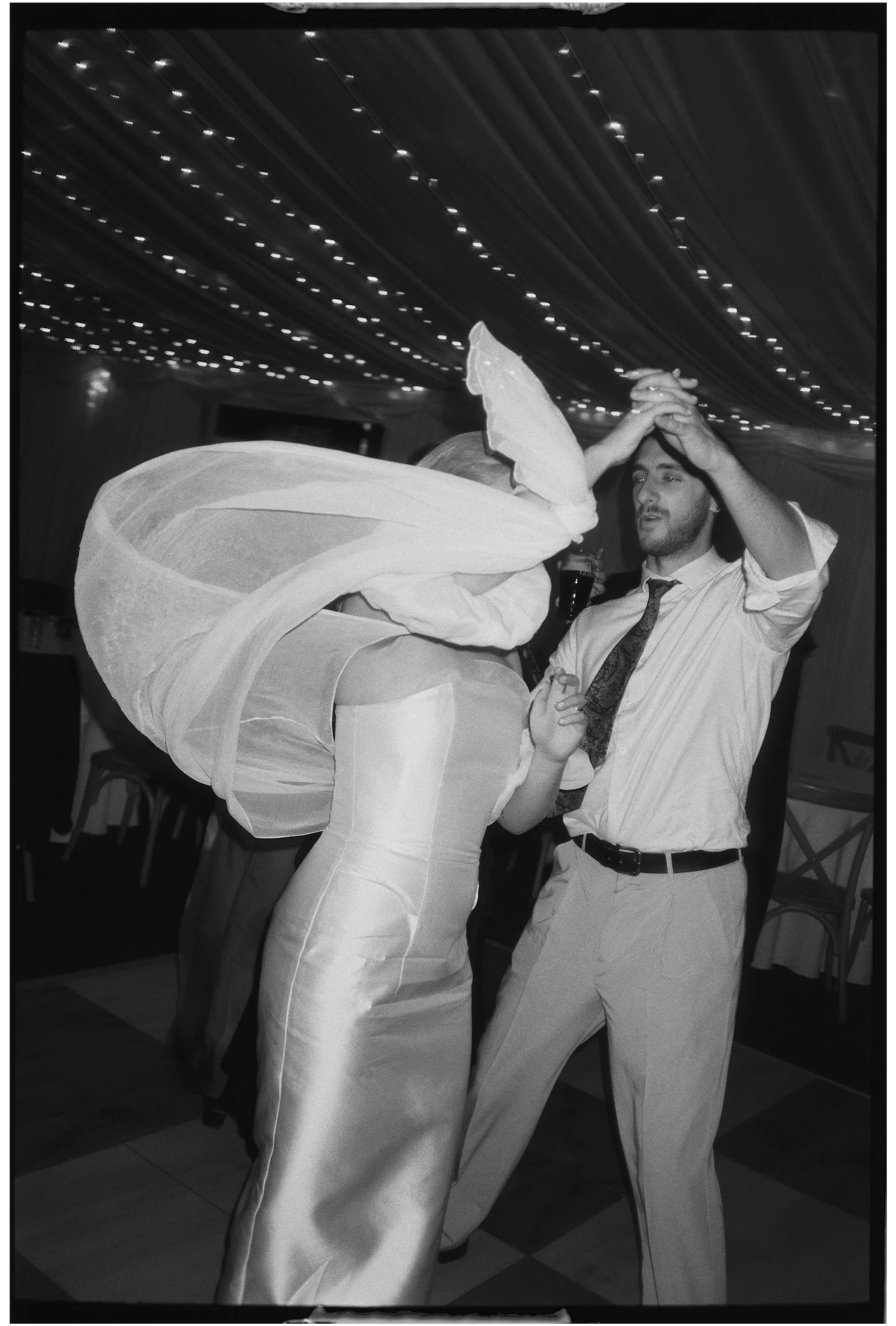 A man and a woman dancing together at a party, with the woman dressed as a fairy with wings and the man wearing a shirt and tie. They are holding hands and appear to be enjoying the dance.