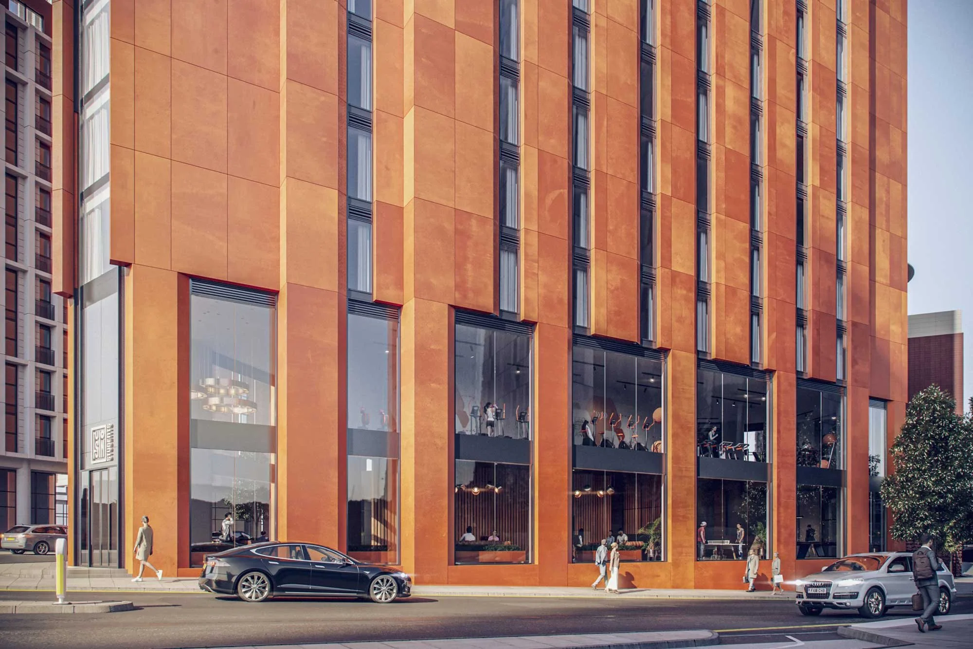 Modern orange brick office building with large glass windows, a gym visible inside, and people walking on the sidewalk in front of it. Several cars are parked along the street.