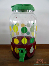 clear plastic tap with fifties-style pears and apples in yellow and green, with a green lid and green spout. filled with a dark pink/purple liquid