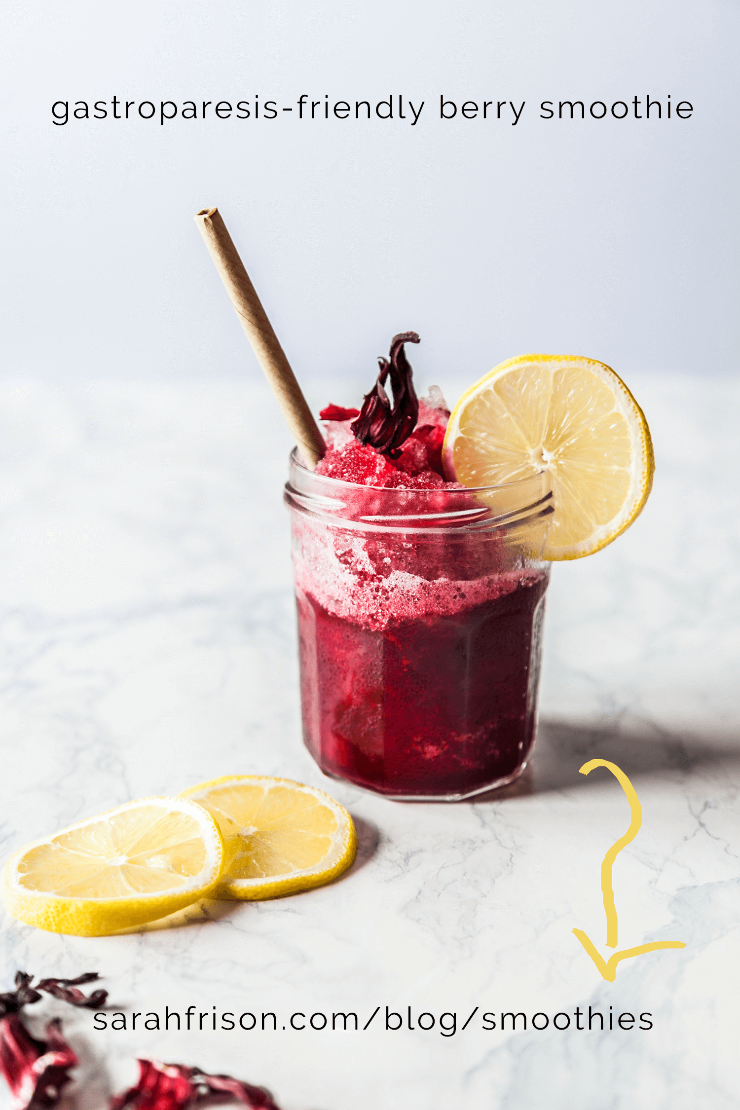 IMAGE: marble worktop with red berry drink in jam jar on it. Jar is finished off with crushed ice, a straw and a slice of lemon on the edge of the glass. There are two more slices of lemon laying on the table. On the image is written 'gastroparesis-friendly berry smoothie, sarahfrison.com/blog/smoothies