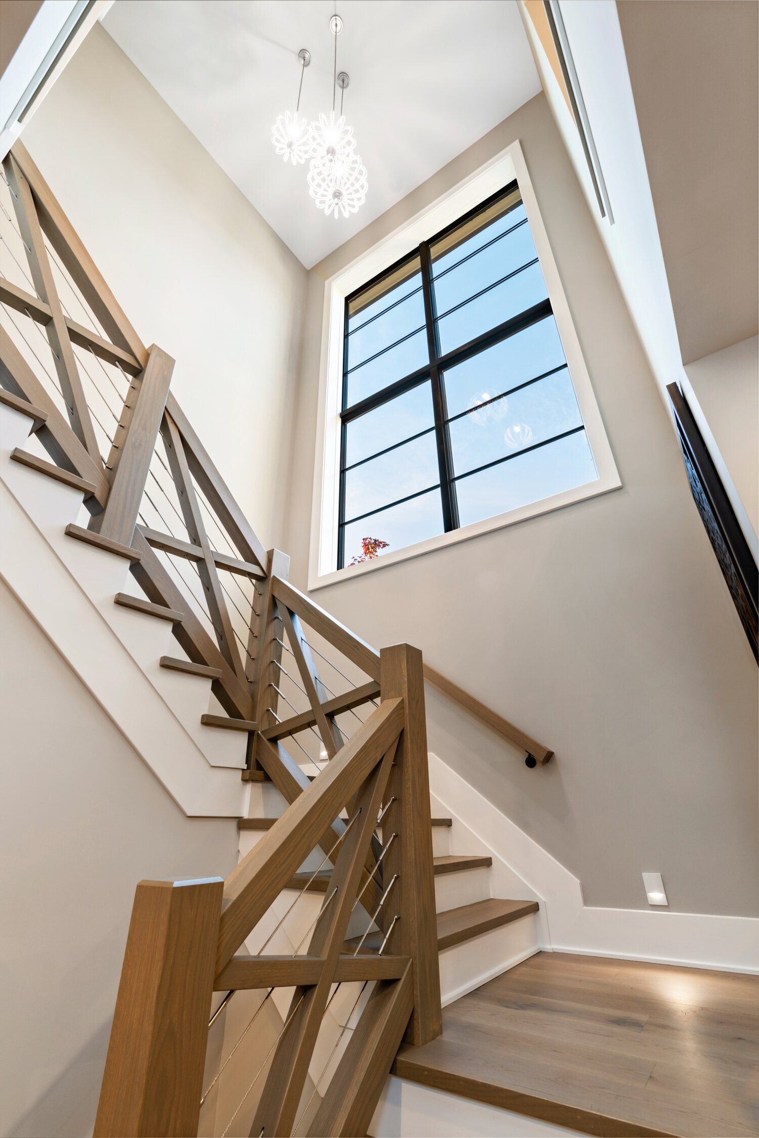 A modern staircase with large windows showcasing an inviting entryway with high ceilings and a sleek chandelier in a custom home.