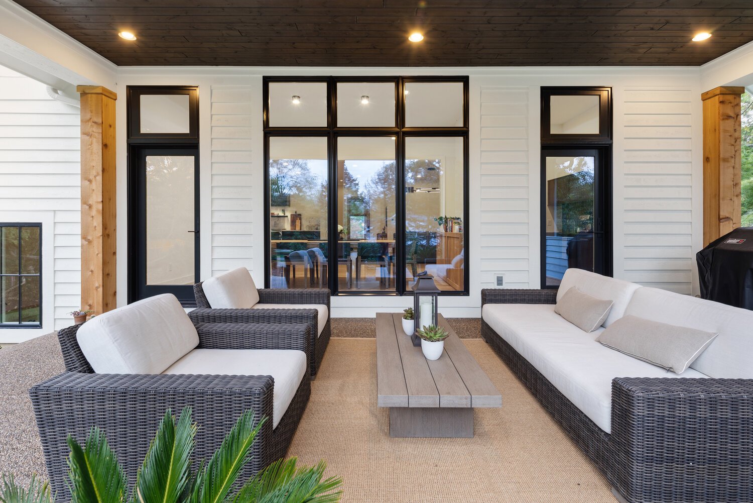 Cozy outdoor living area with wicker furniture and large windows overlooking patio
