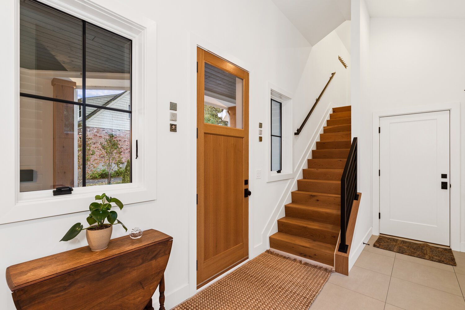 Entryway of modern home with wood staircase, potted plant, and large front door