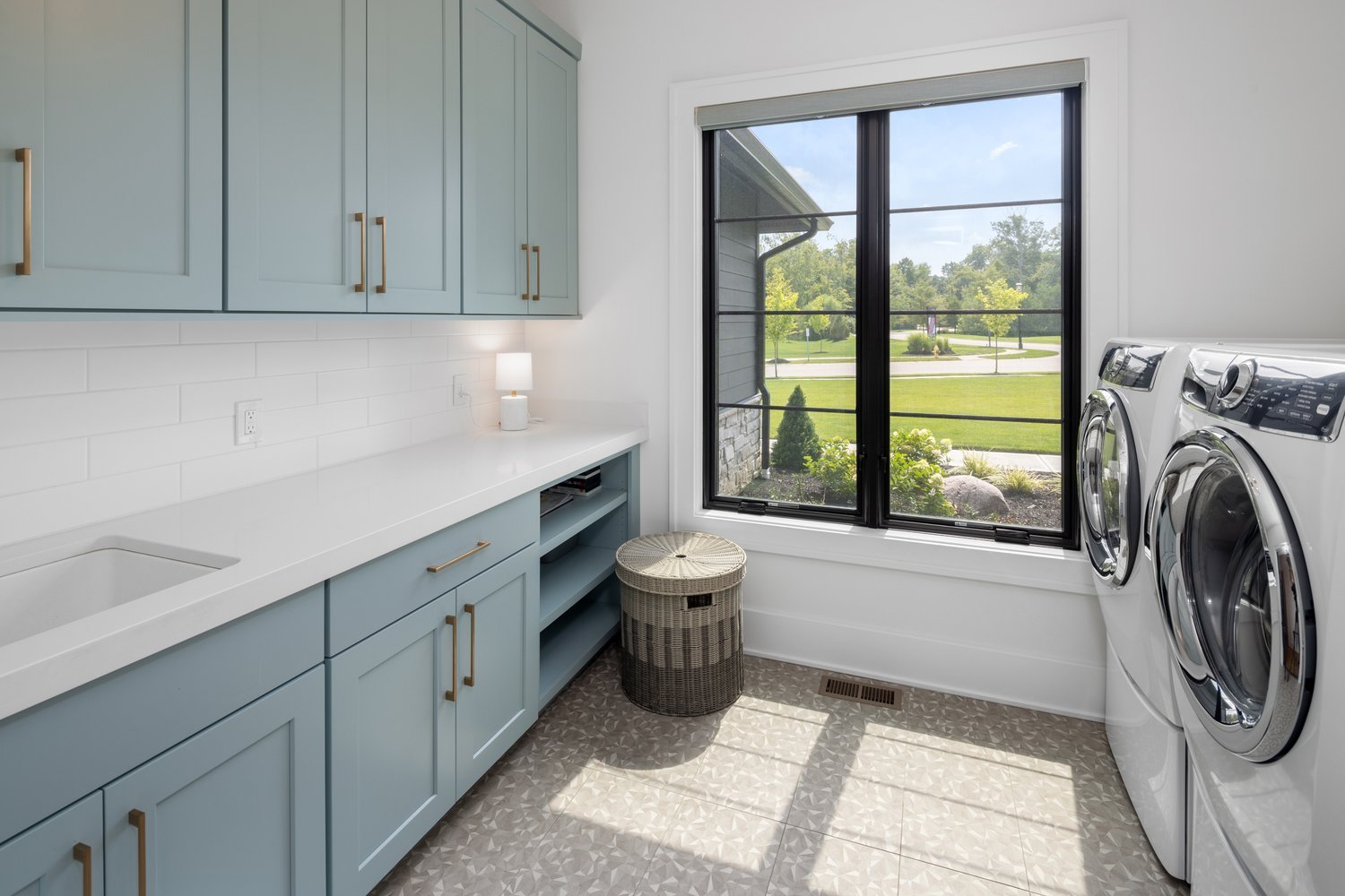 Modern laundry room with sleek cabinets, tiled floors, and a large window overlooking a lush backyard.