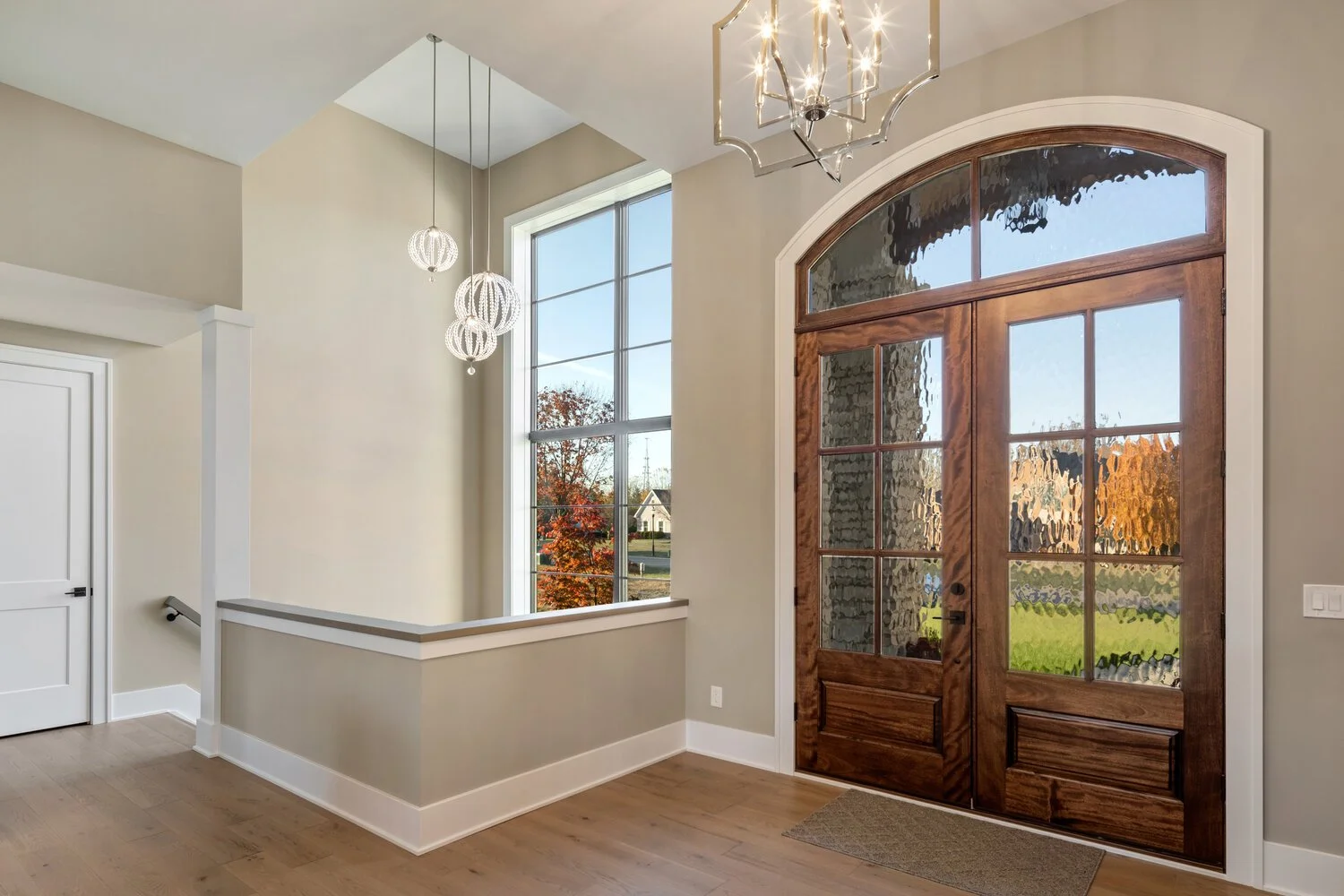 A bright entryway featuring an arched wooden door with glass panes, providing natural light, and elegant light fixtures creating a warm and inviting first impression.