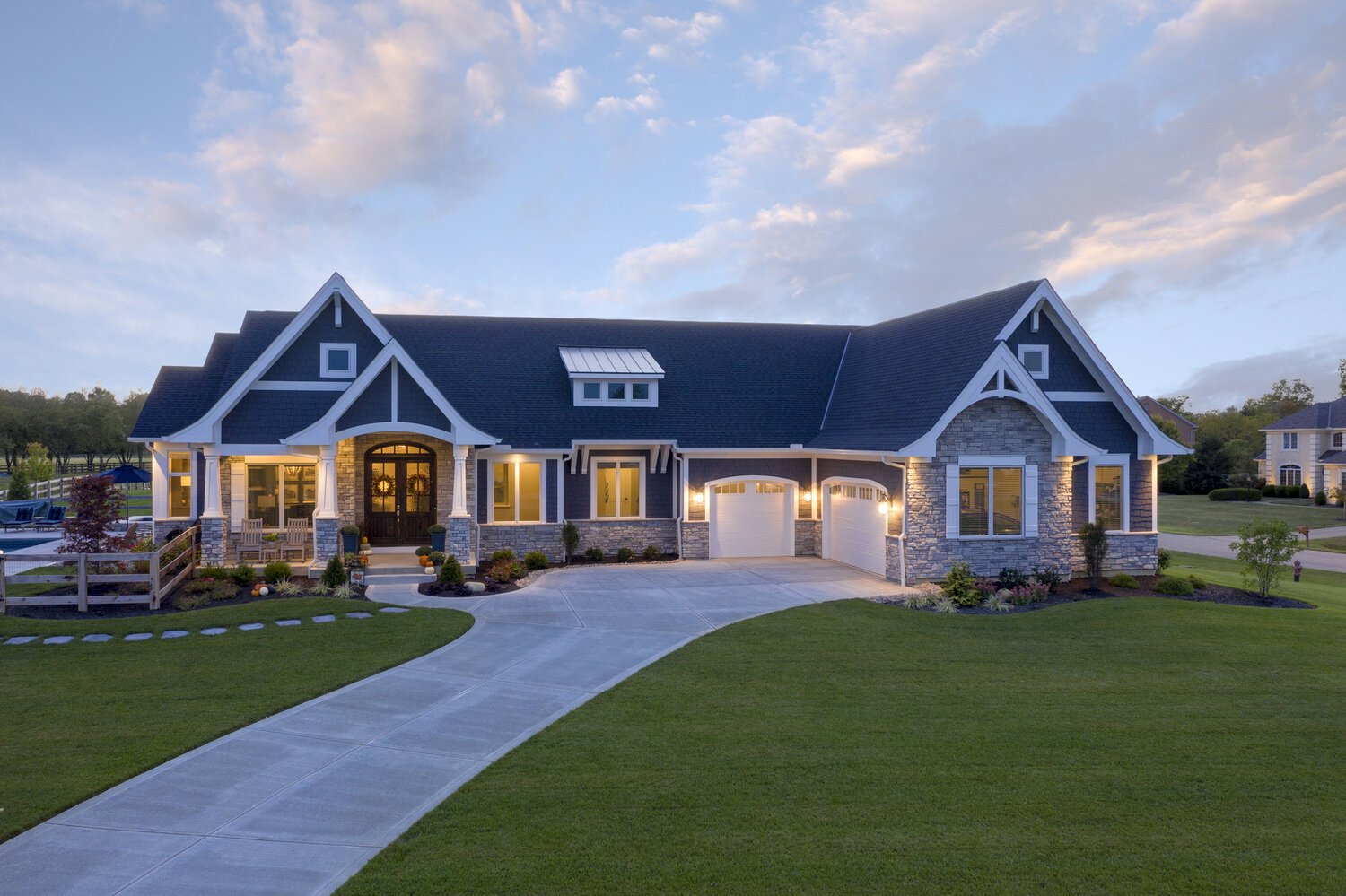 Exterior view of a luxurious custom-built home with a stone and wood facade, featuring a large covered porch and landscaped front yard.