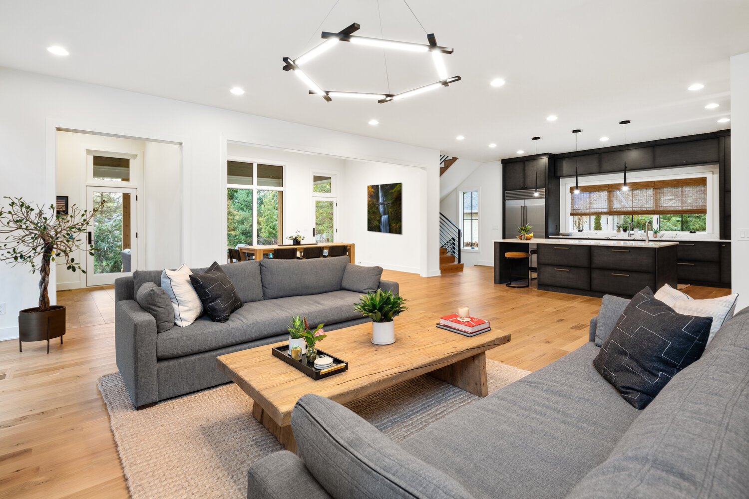 Open concept living space with gray sofas, hardwood floors, and kitchen visible