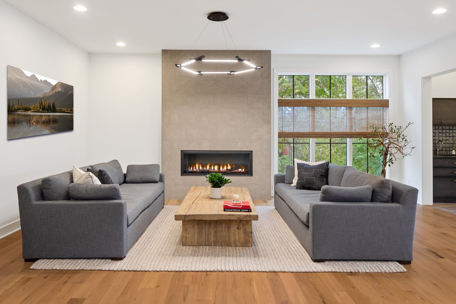 Modern living room with fireplace, gray sofas, wood coffee table overlooking wooded view