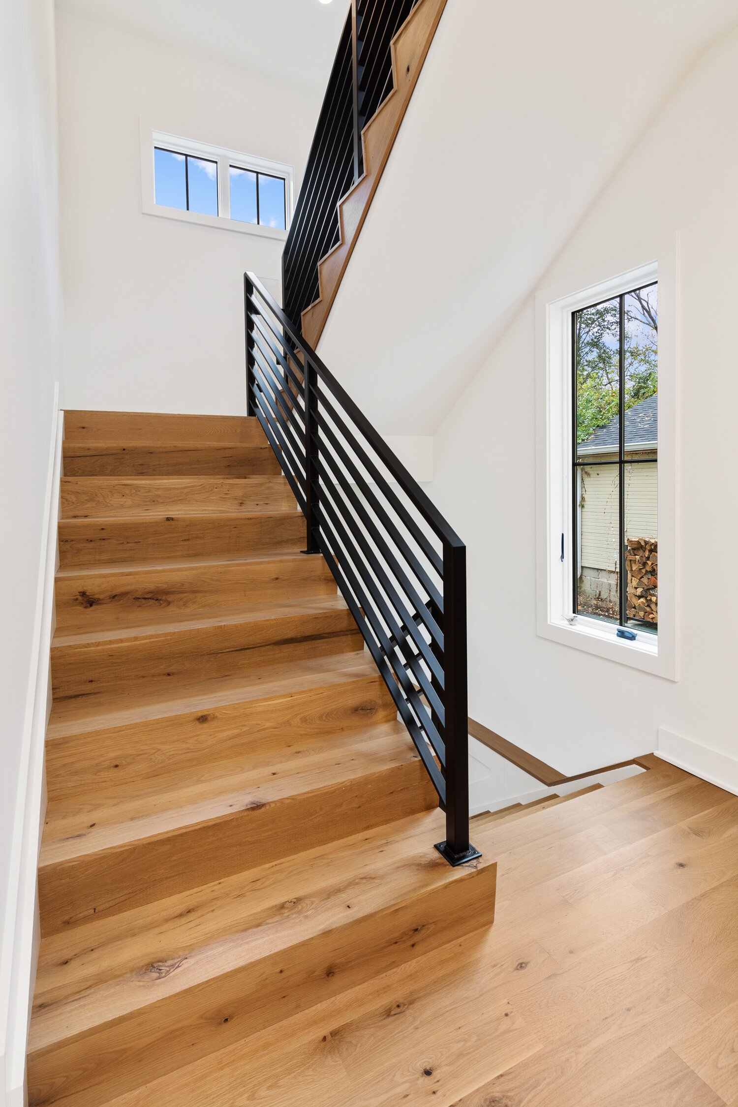 Wooden staircase with metal railing leads upstairs, featuring window with wood storage pile view