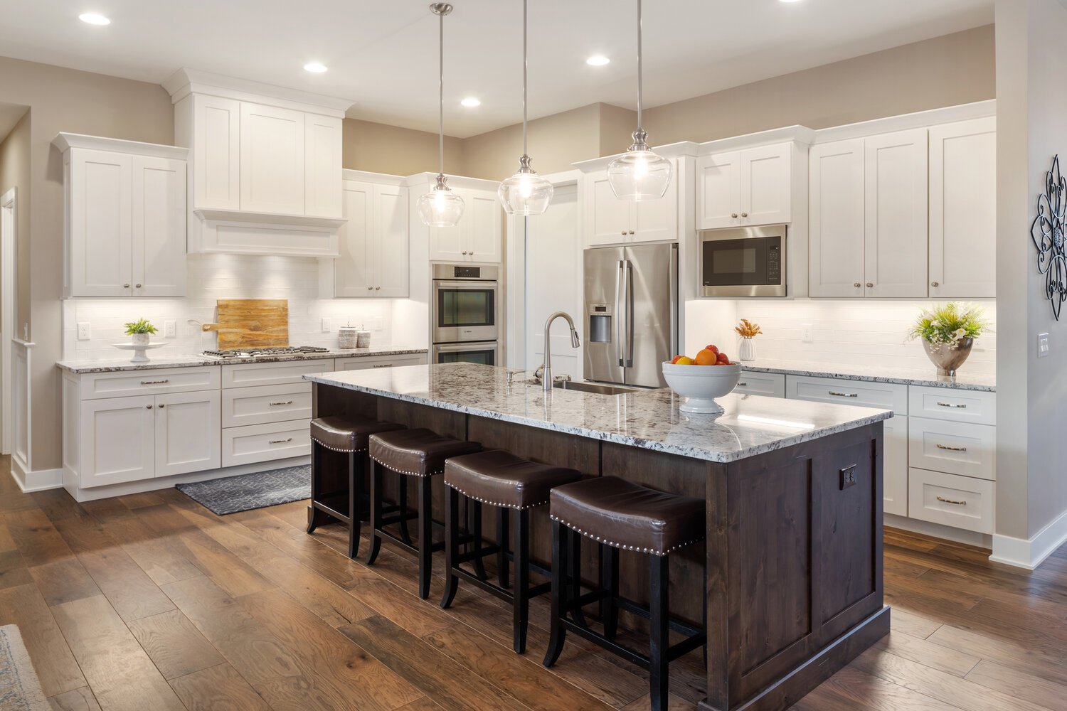 Spacious and modern kitchen with white cabinetry, a large island with a granite countertop and bar seating, and high-end stainless steel appliances.