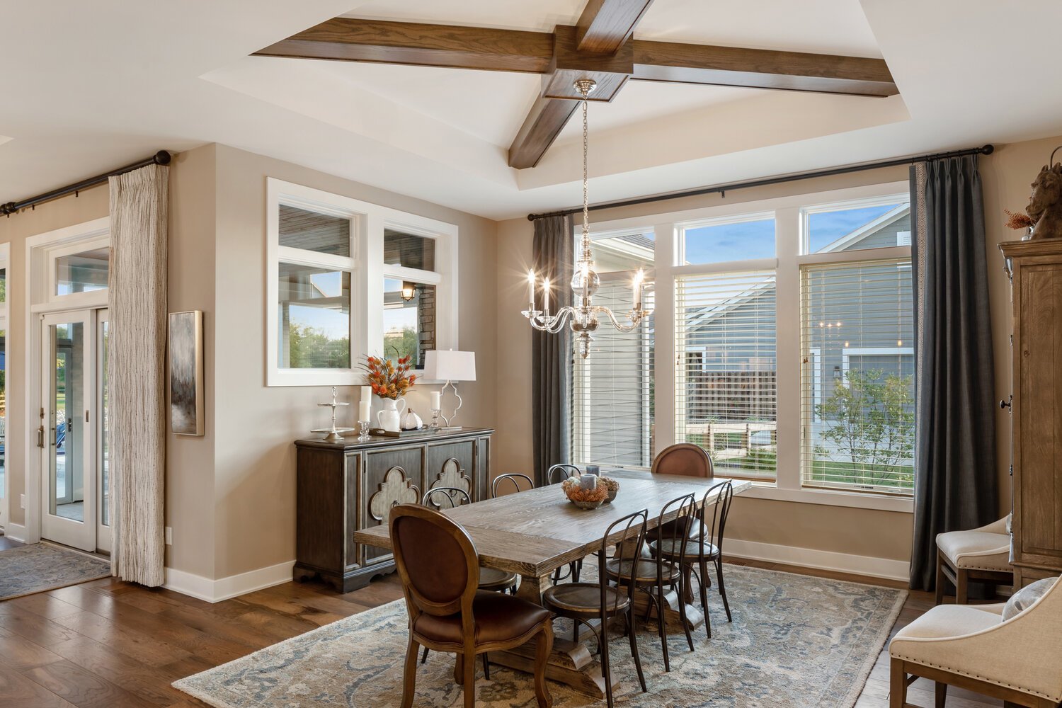 Bright and airy dining room with large windows, a wooden ceiling fan, a chandelier, and a wooden table set for a stylish gathering.