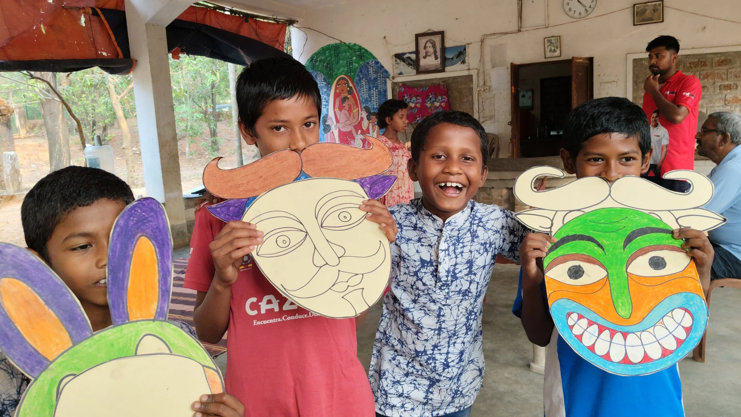 Children holding colorful masks in a classroom with decorations and pictures on the walls.