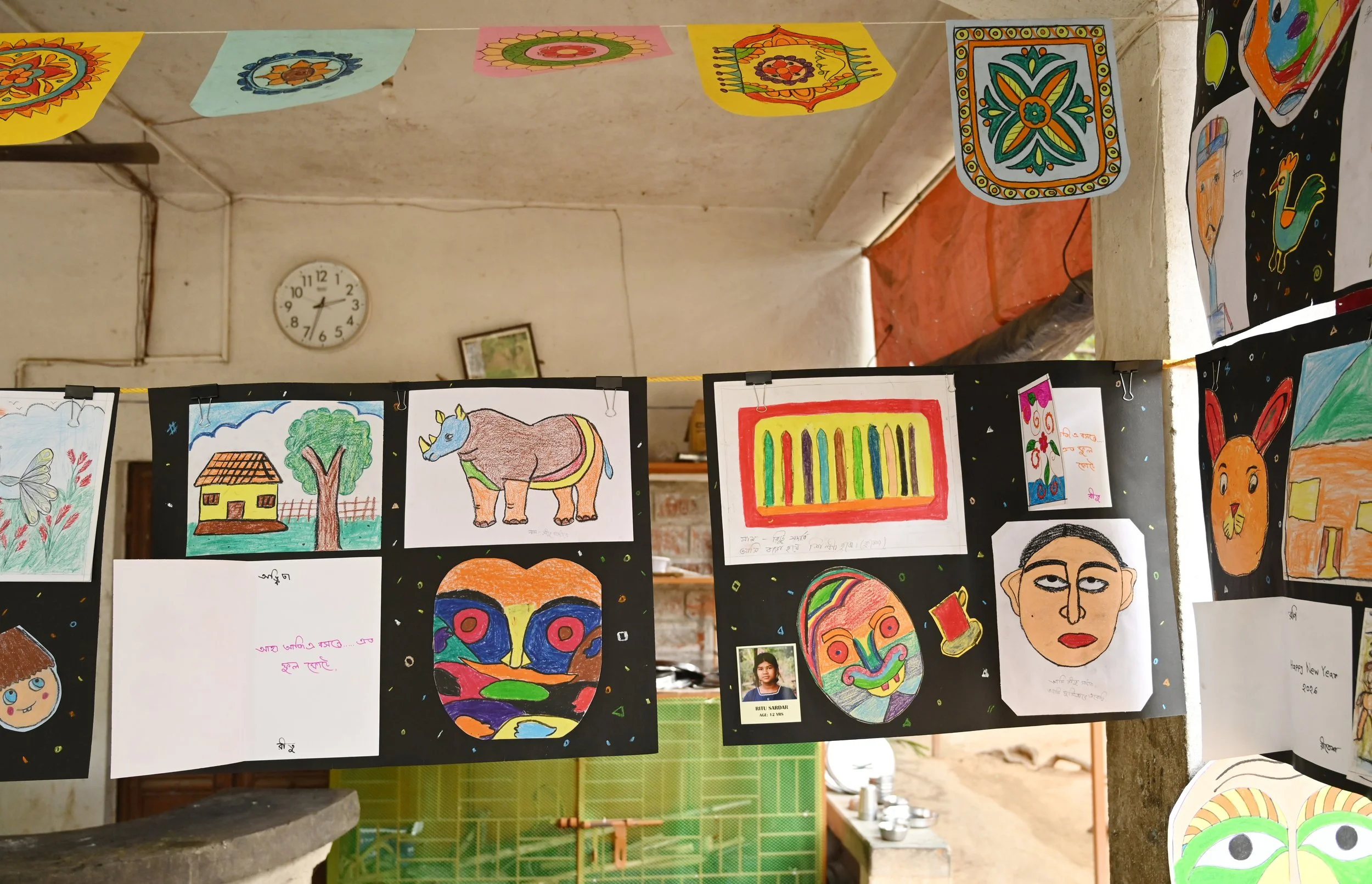 Colorful drawings hanging on strings inside a room, including a house, a tree, an elephant, a butterfly, face sketches, and abstract designs.