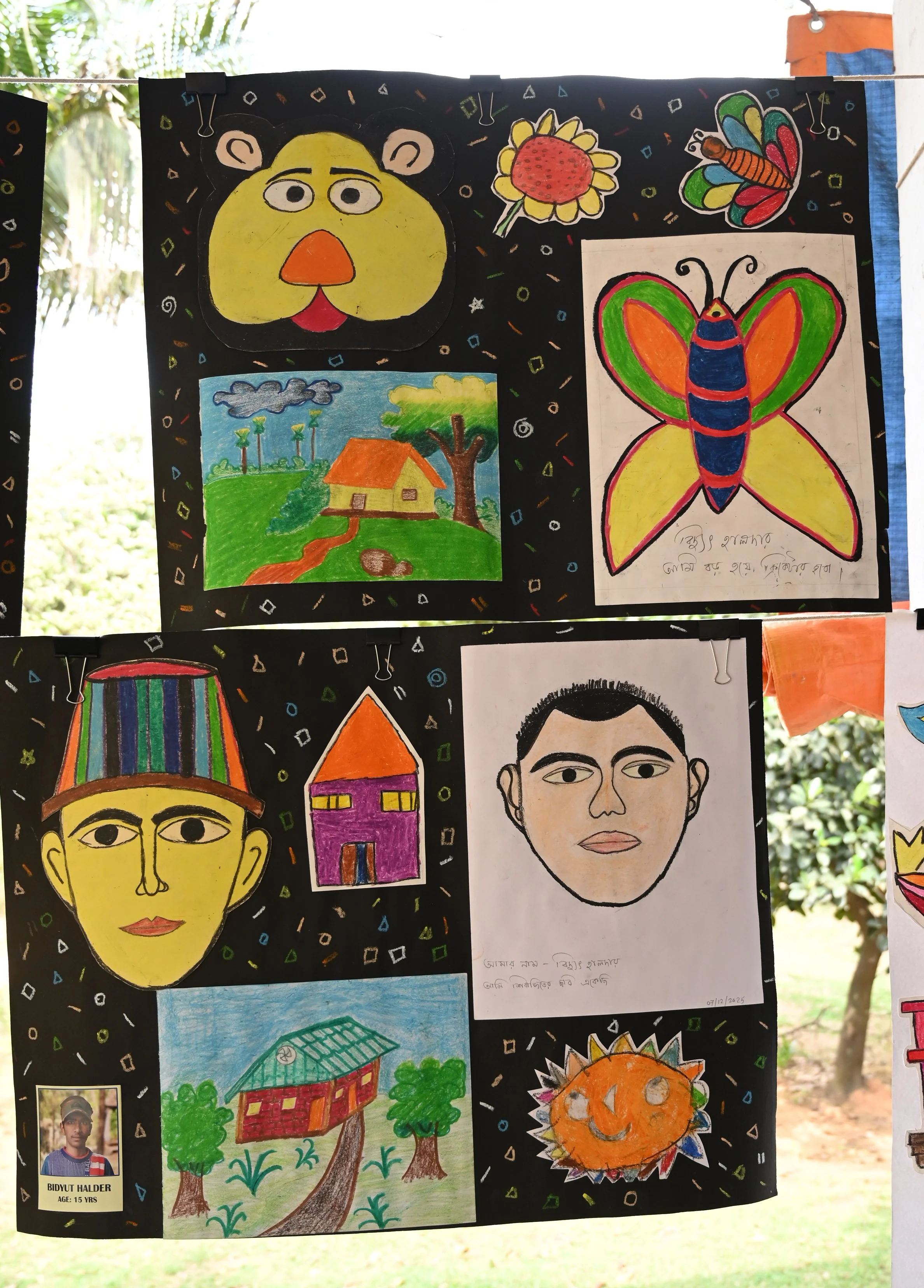 Colorful drawings on black paper showing a bear's face, a house with trees, a butterfly, a sunflower, and a smiling sun, with doodles and signatures.