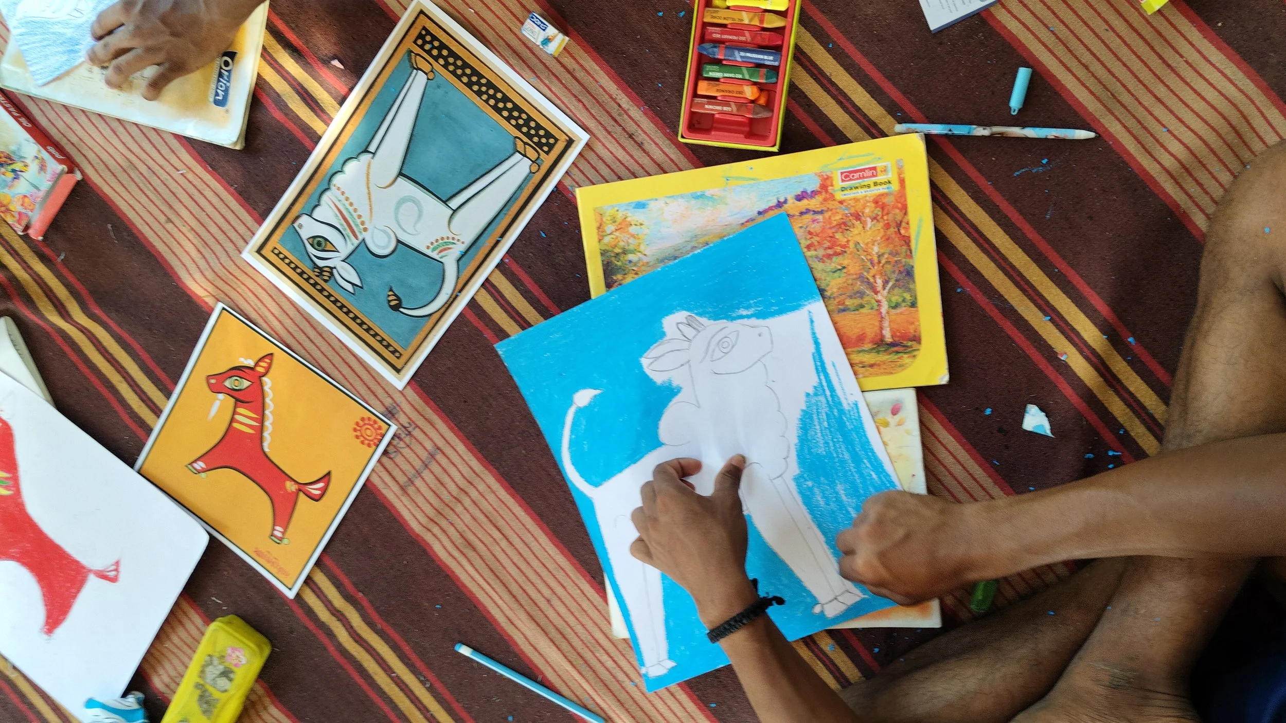 People coloring pictures of animals, including a dog and a horse, on a patterned blanket with coloring supplies scattered around.