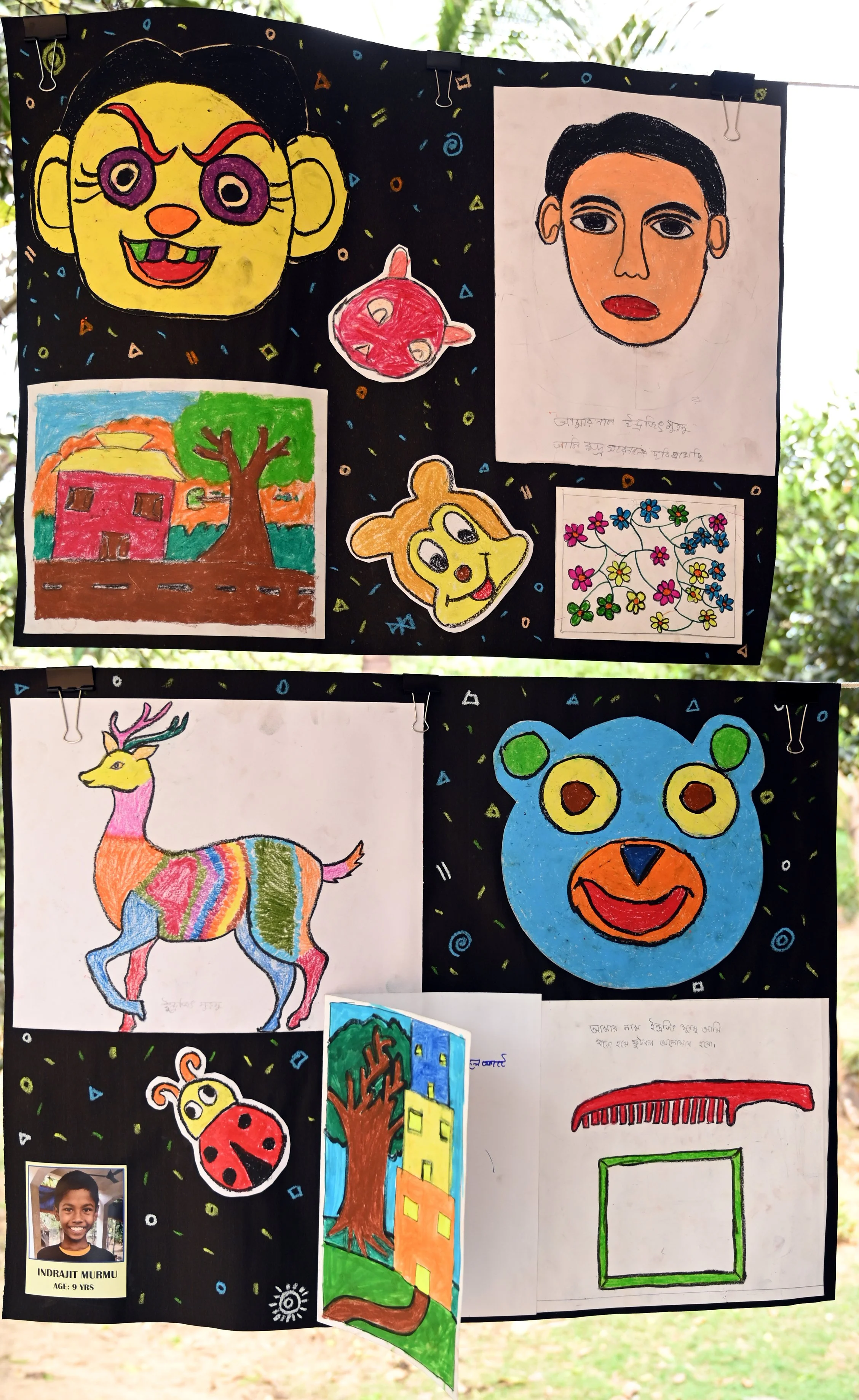 A display board of children's artwork with colorful drawings of faces, animals, houses, and abstract designs, featuring a photo of a young boy named Indrajit Murmu, aged 9.