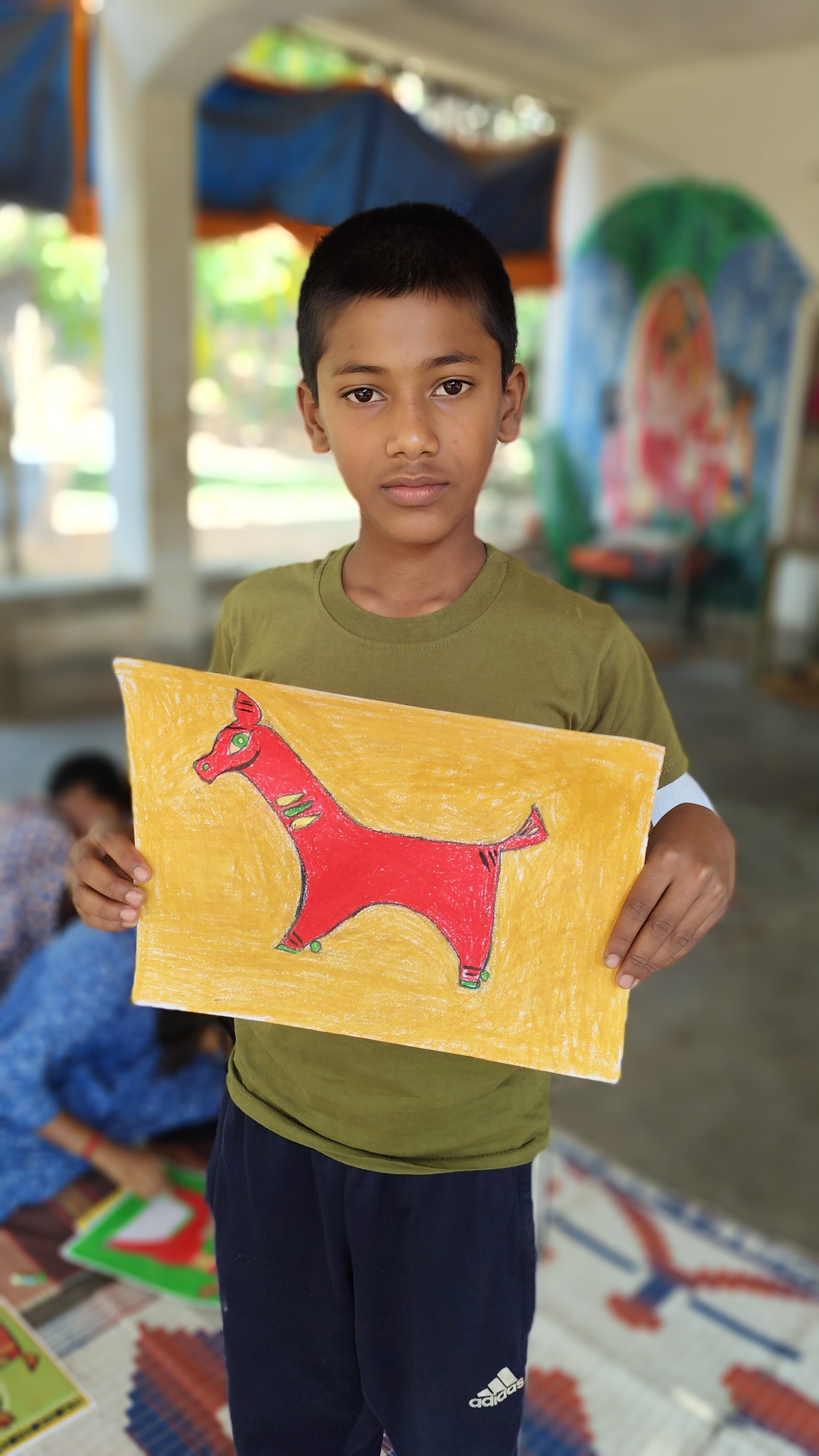 Young boy in green shirt holding a brightly colored drawing of a red horse against a yellow background.