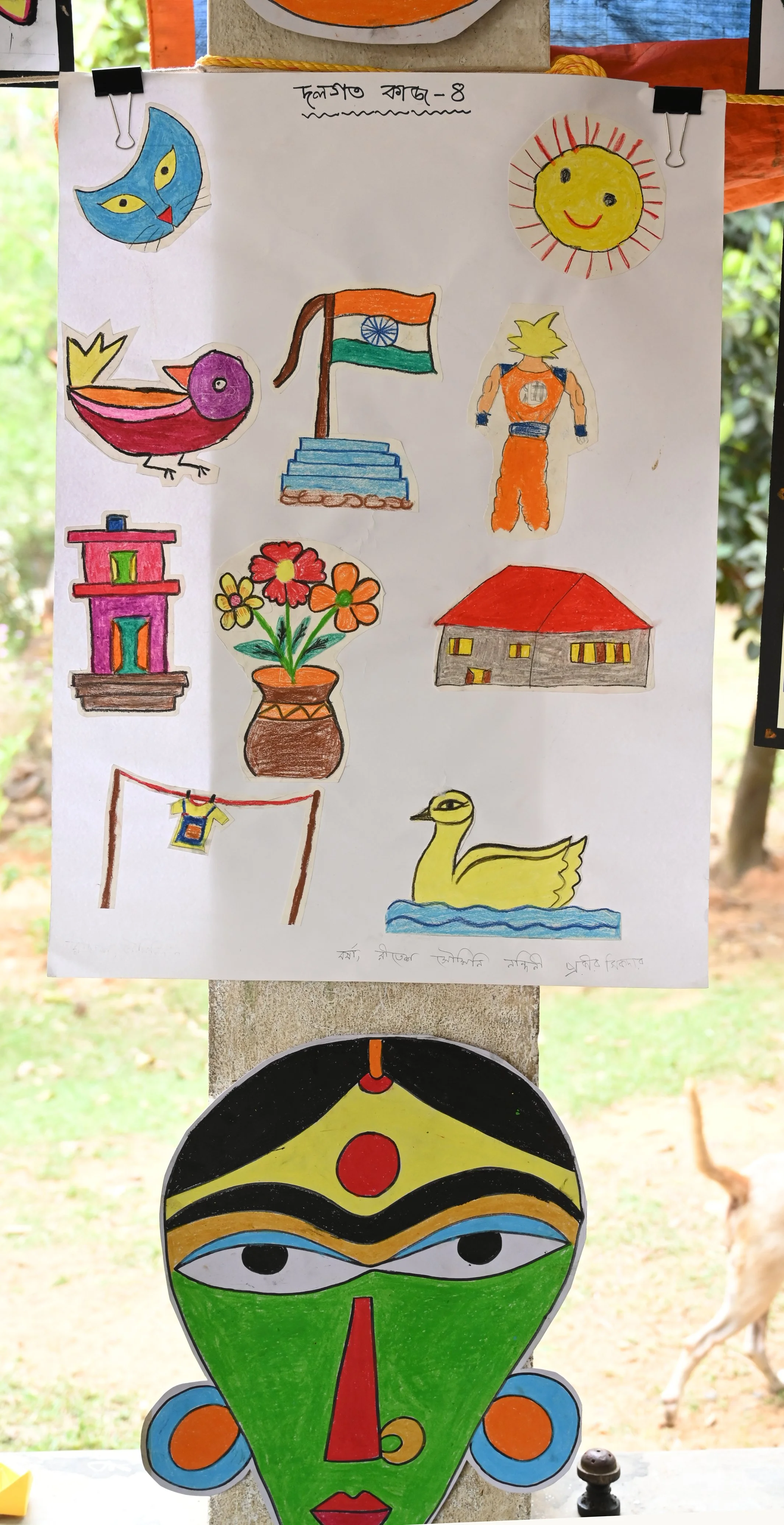 Colorful drawings depicting various objects and characters including a blue cat face, the sun with a smiling face, a pink and purple bird, the Indian flag, a person in an orange outfit, a house with a red roof, a pot of flowers, a clothesline with a 