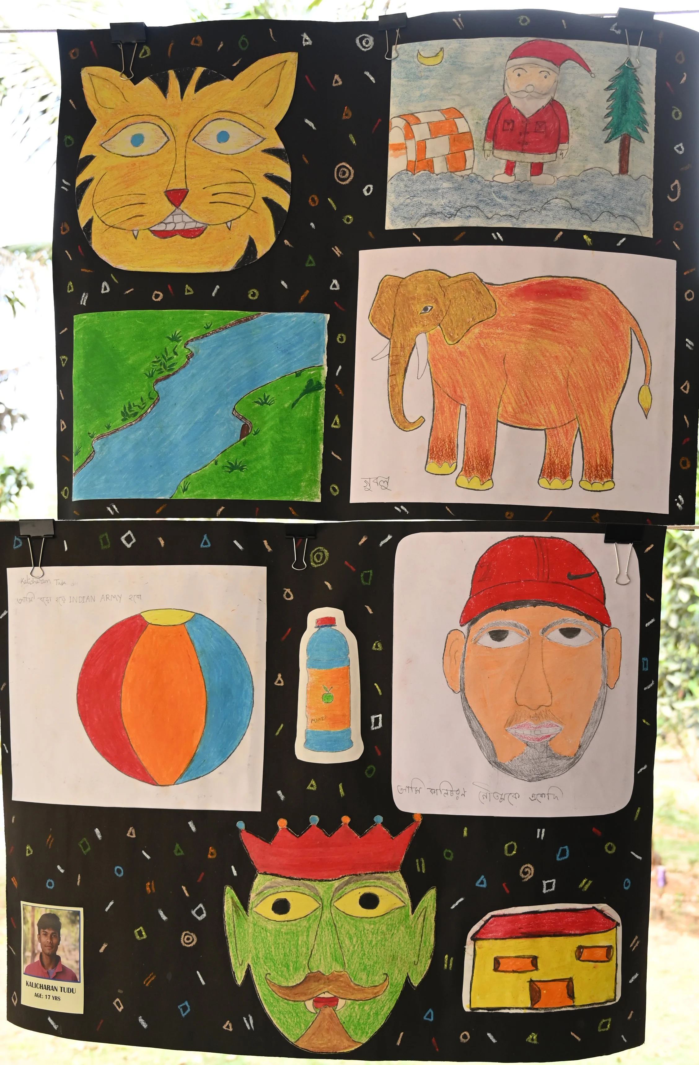 Colorful children's drawings displayed on a black background with small, colorful confetti-like patterns. The artwork includes a lion's face, a landscape with a river and grass, a Santa Claus figure, an elephant, a hot air balloon, a cartoon-like fac